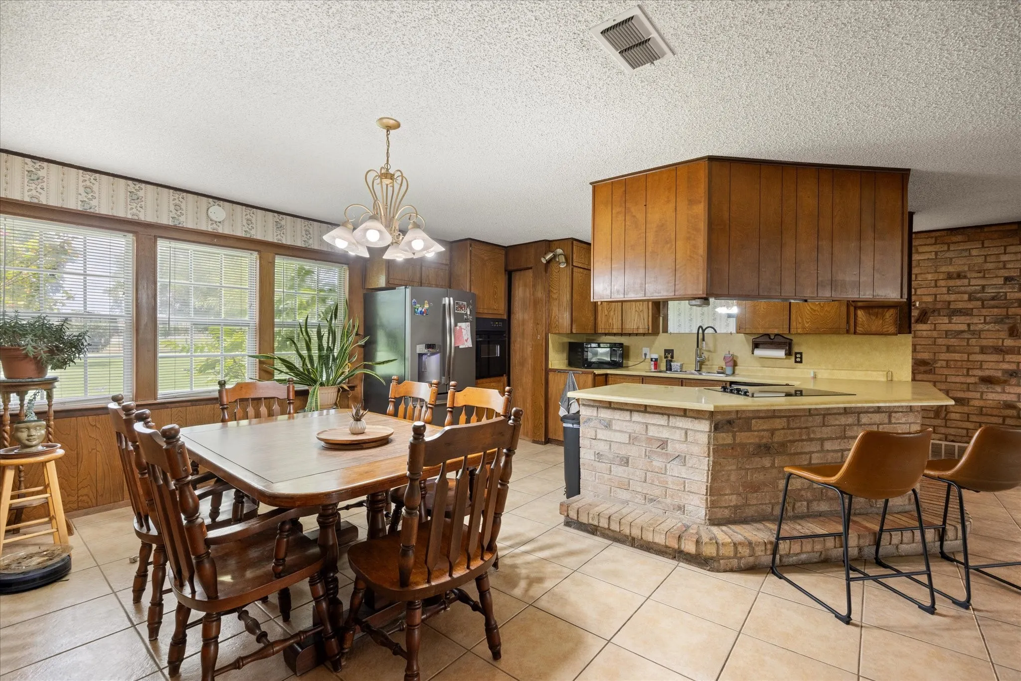 Kitchen and dining area featuring tile flooring, wood-finish paneling, and an exposed brick accent wall