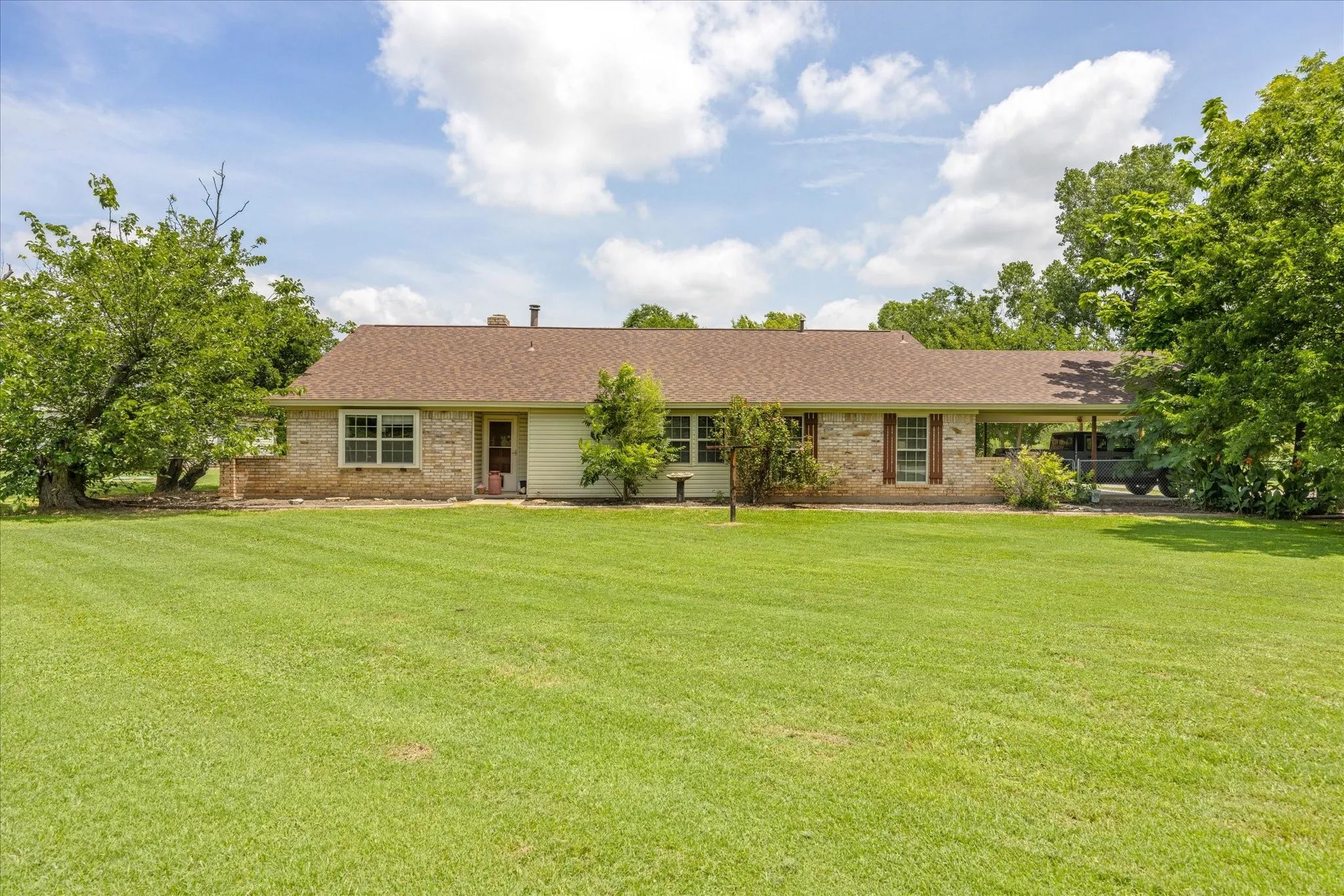 Ranch-style residence featuring a brick facade, covered carport, and a brown shingle roof