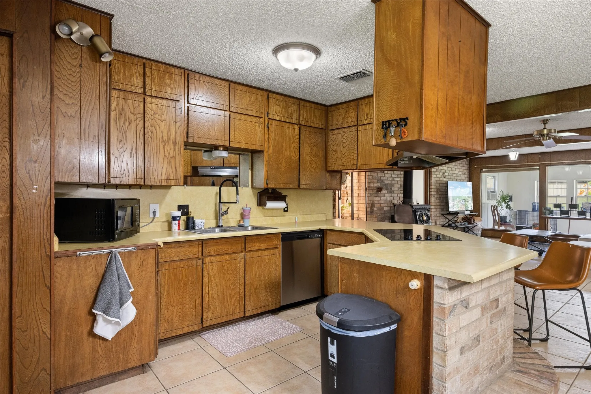Kitchen featuring wood cabinetry, a built-in cooktop on an island, an undermount sink with a gooseneck faucet, stainless steel dishwasher, and tile flooring