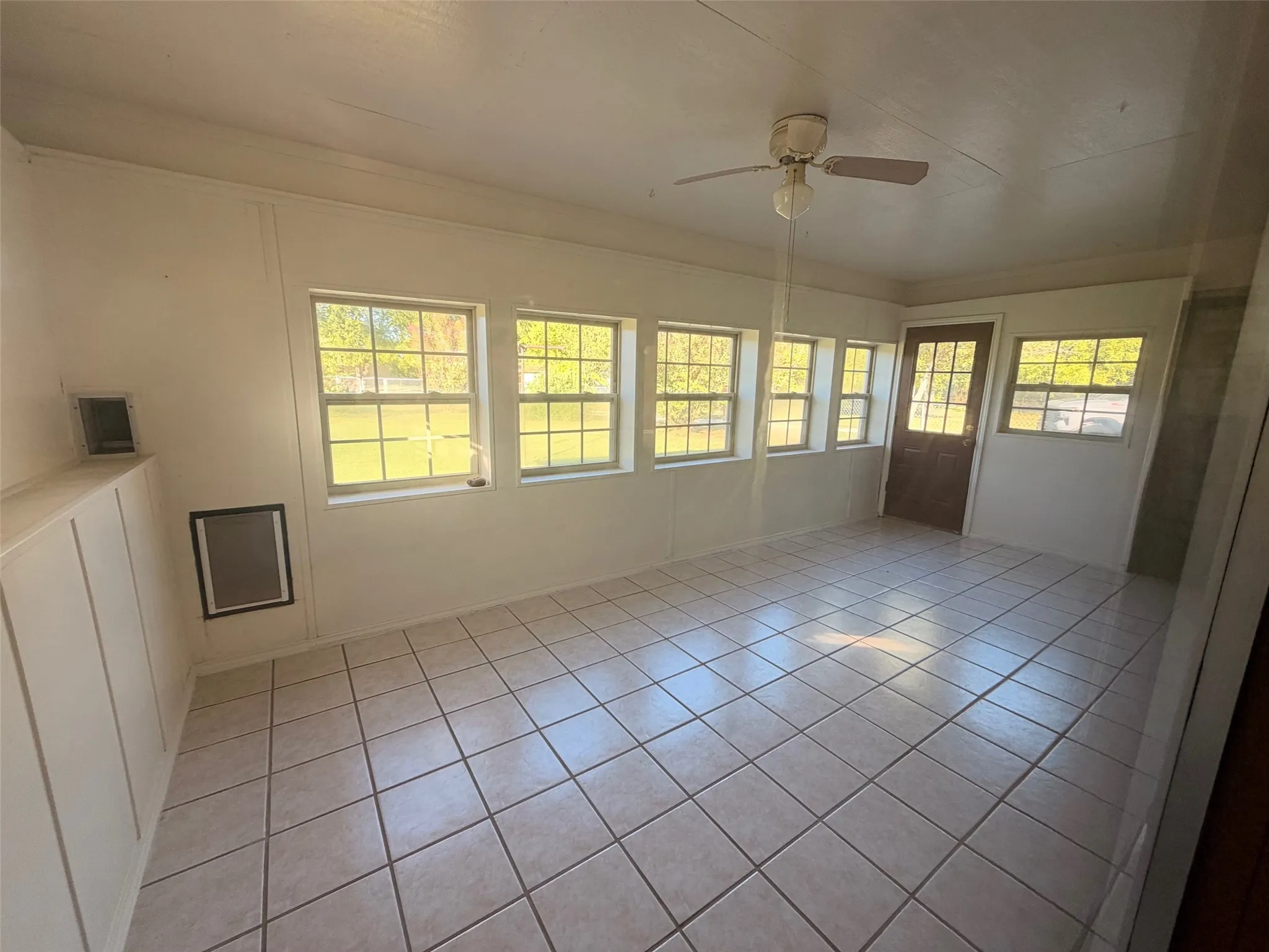 Ceramic tile flooring, multiple windows, ceiling fan, paneled walls, and a glass-paneled door