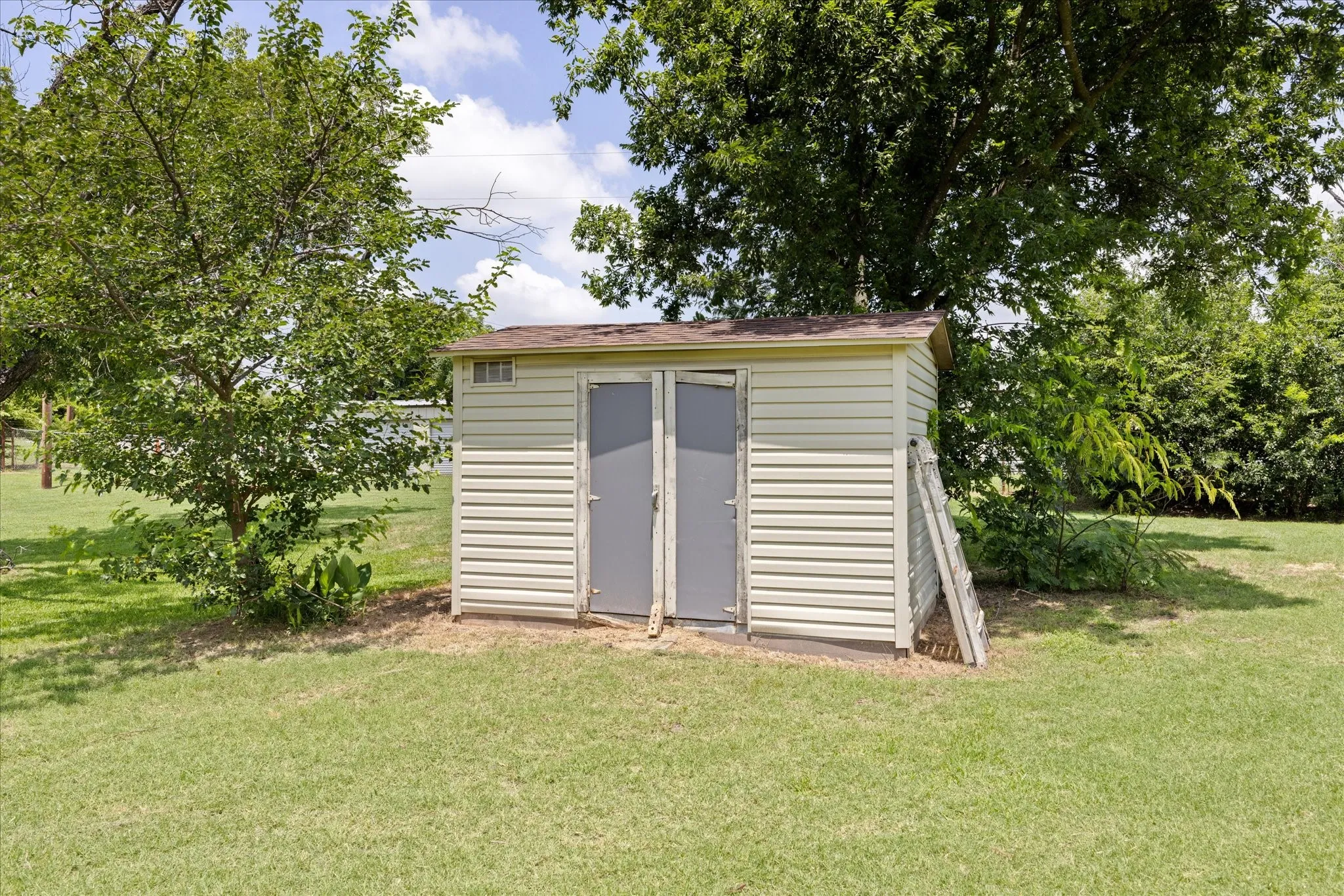 Storage shed featuring light-colored siding, dual panel doors, and a shingled roof