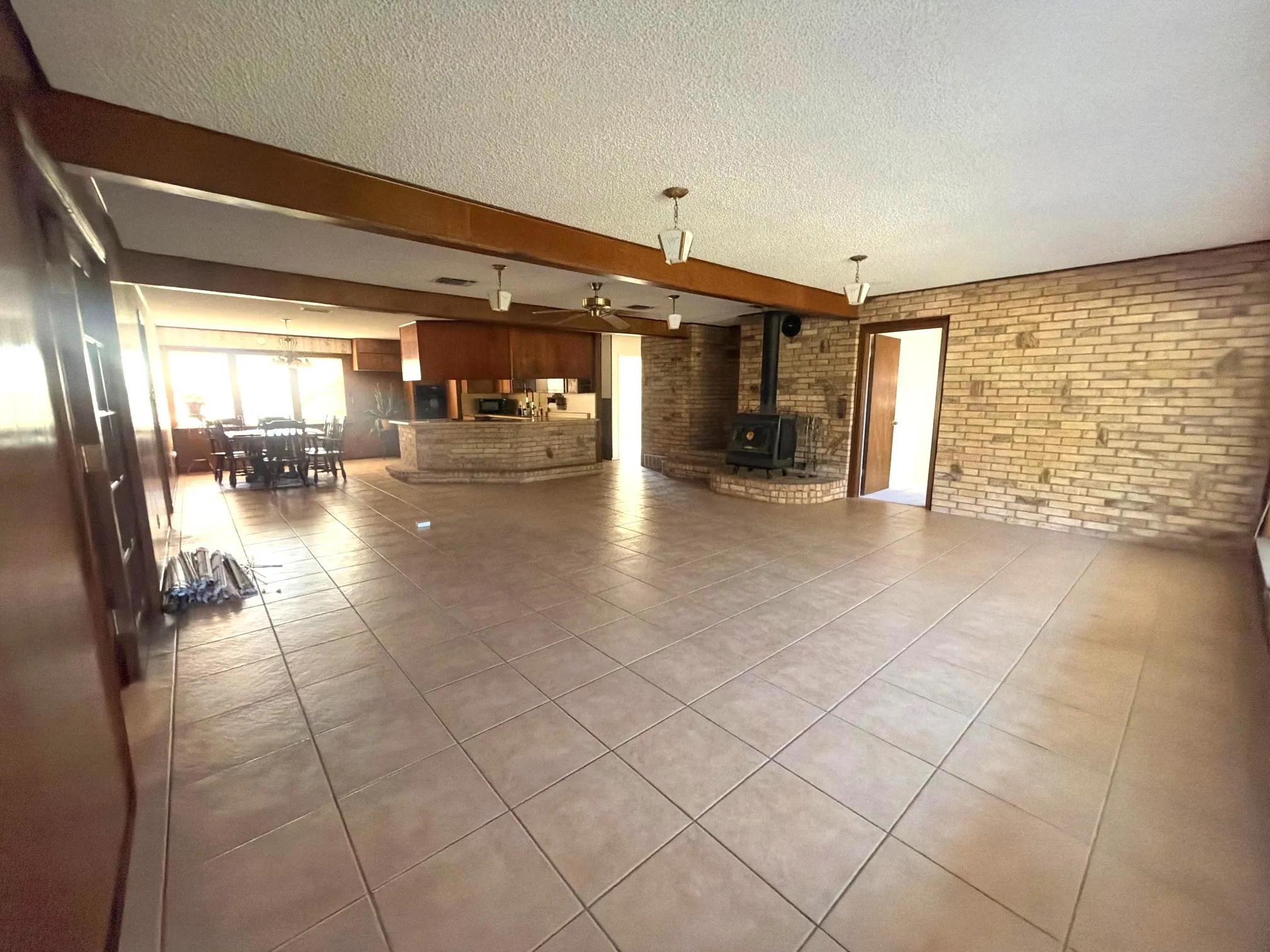 Tile flooring, exposed wood beams, brick accent walls, kitchen island with built-in cabinetry, and a wood-burning stove