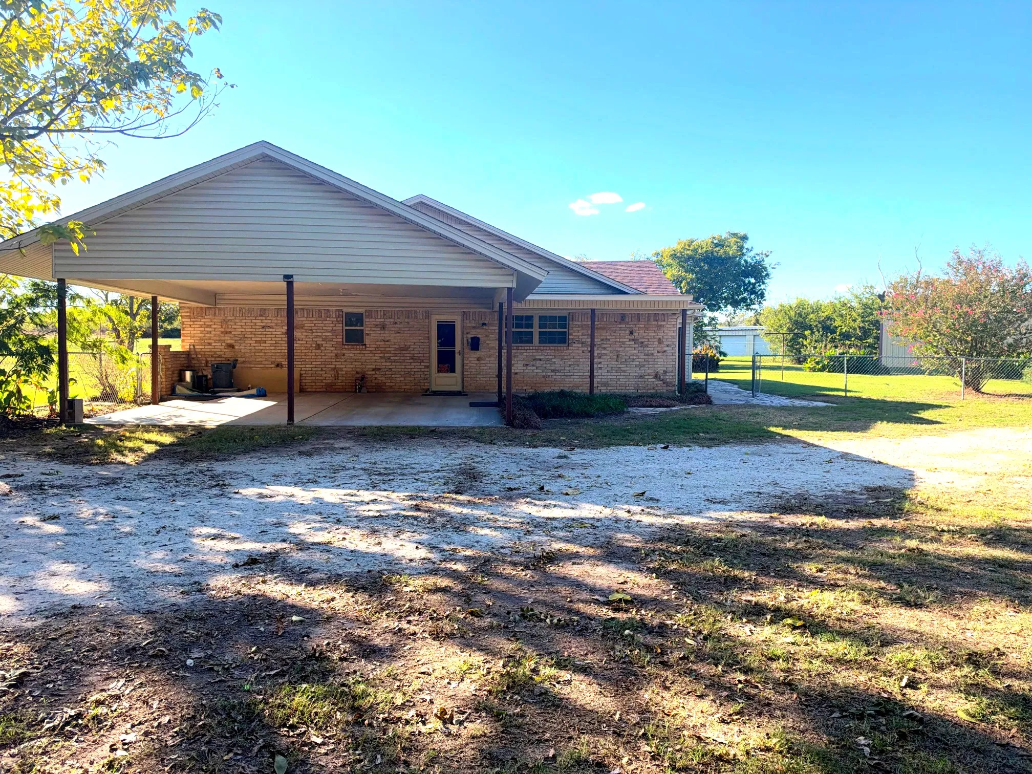 Brick exterior featuring a covered carport, covered porch, and a fenced backyard