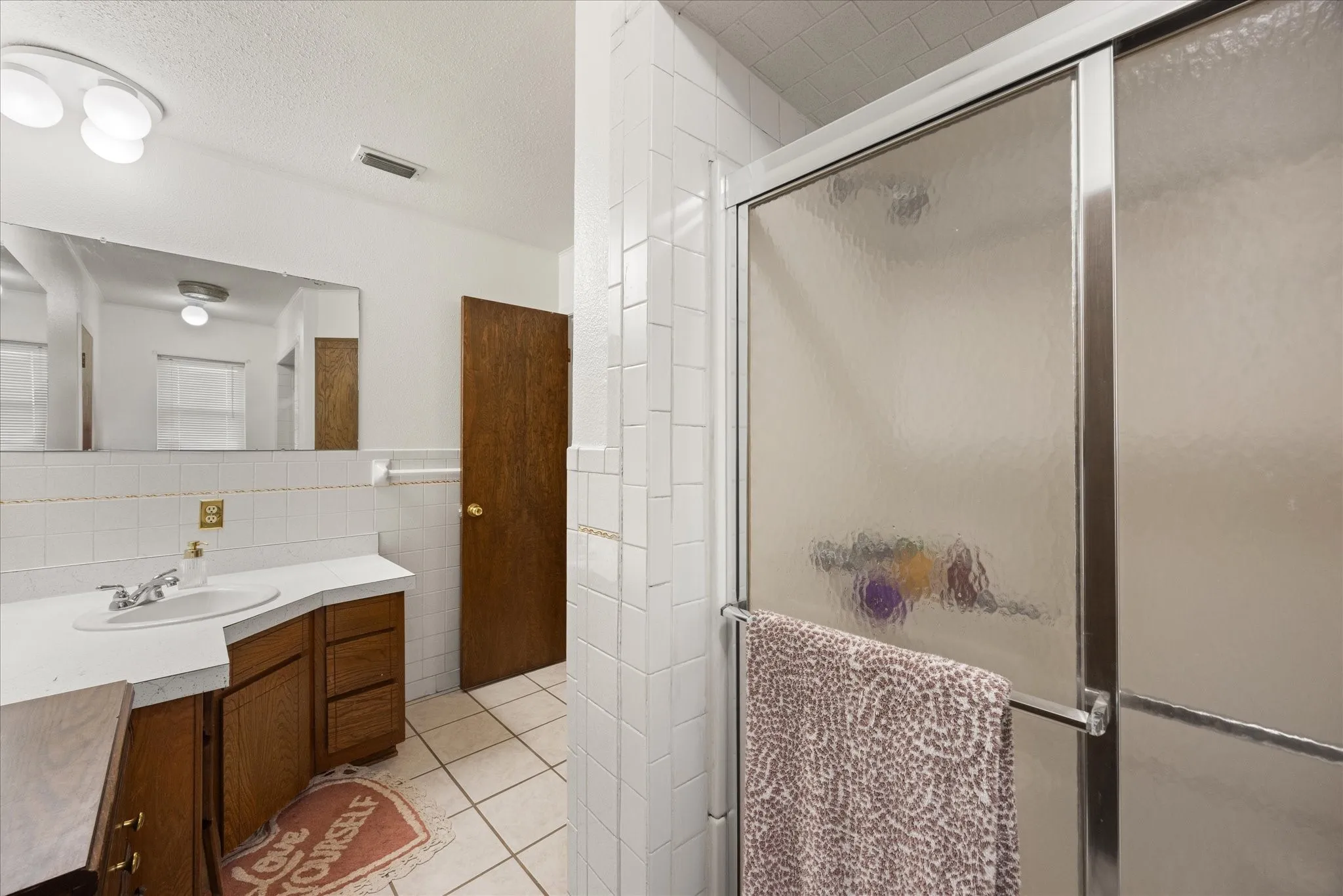 Bathroom featuring a tiled shower with sliding frosted glass doors, a single vanity with wood-finish cabinetry, a white countertop, and a large wall-mounted mirror