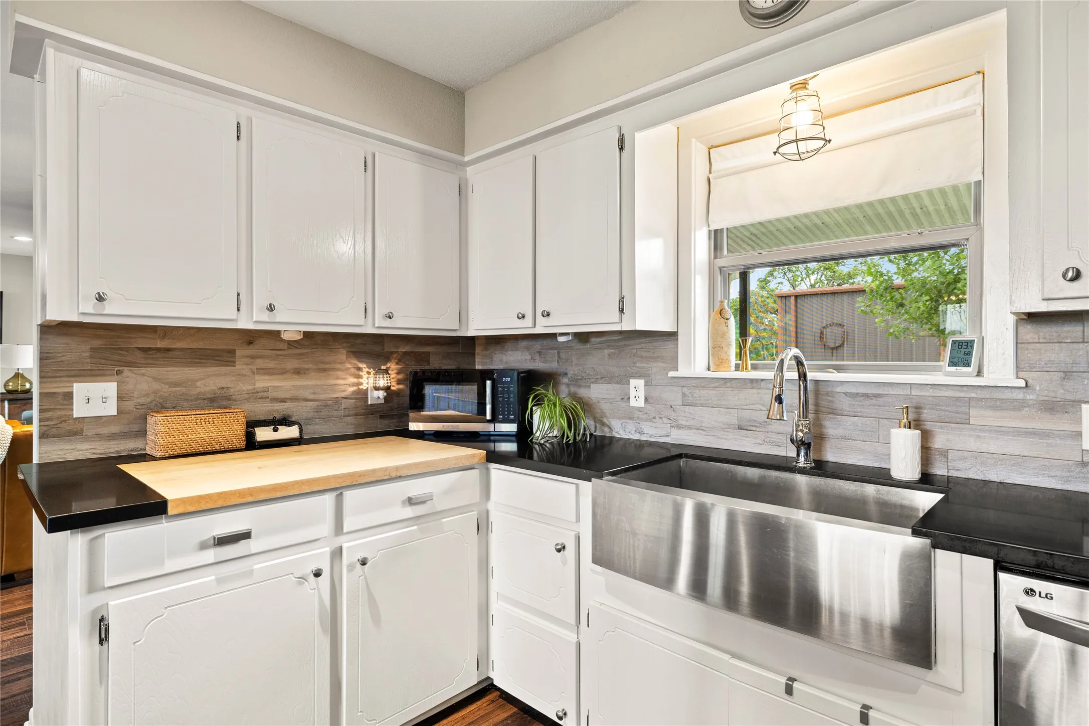 Kitchen featuring white cabinetry, dark countertops, a large farmhouse-style stainless steel sink, a modern pull-down faucet, and a wood-finish backsplash