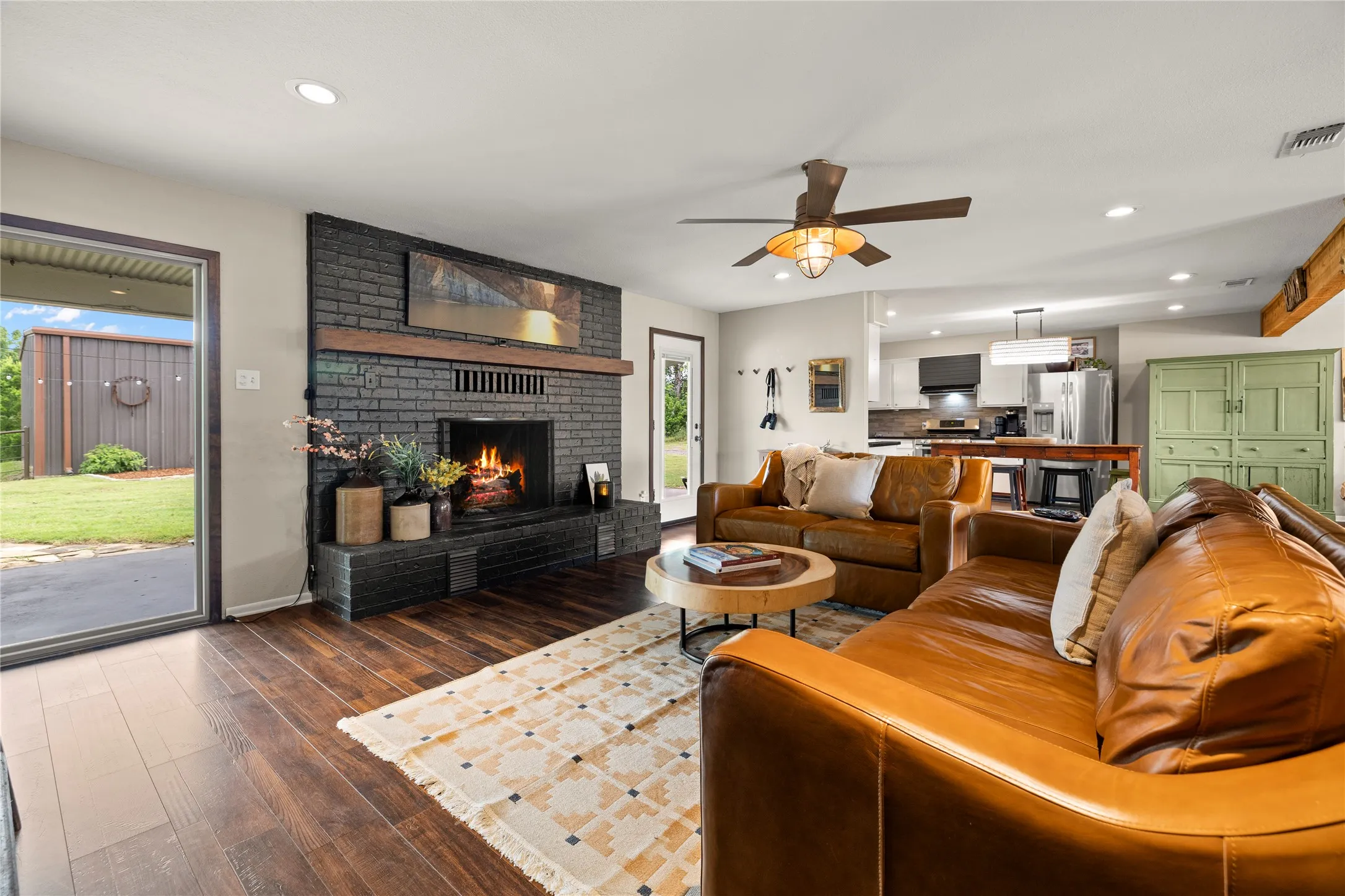Living area featuring a dark brick fireplace with a wood mantle, wood-finish flooring, a ceiling fan, and recessed lighting