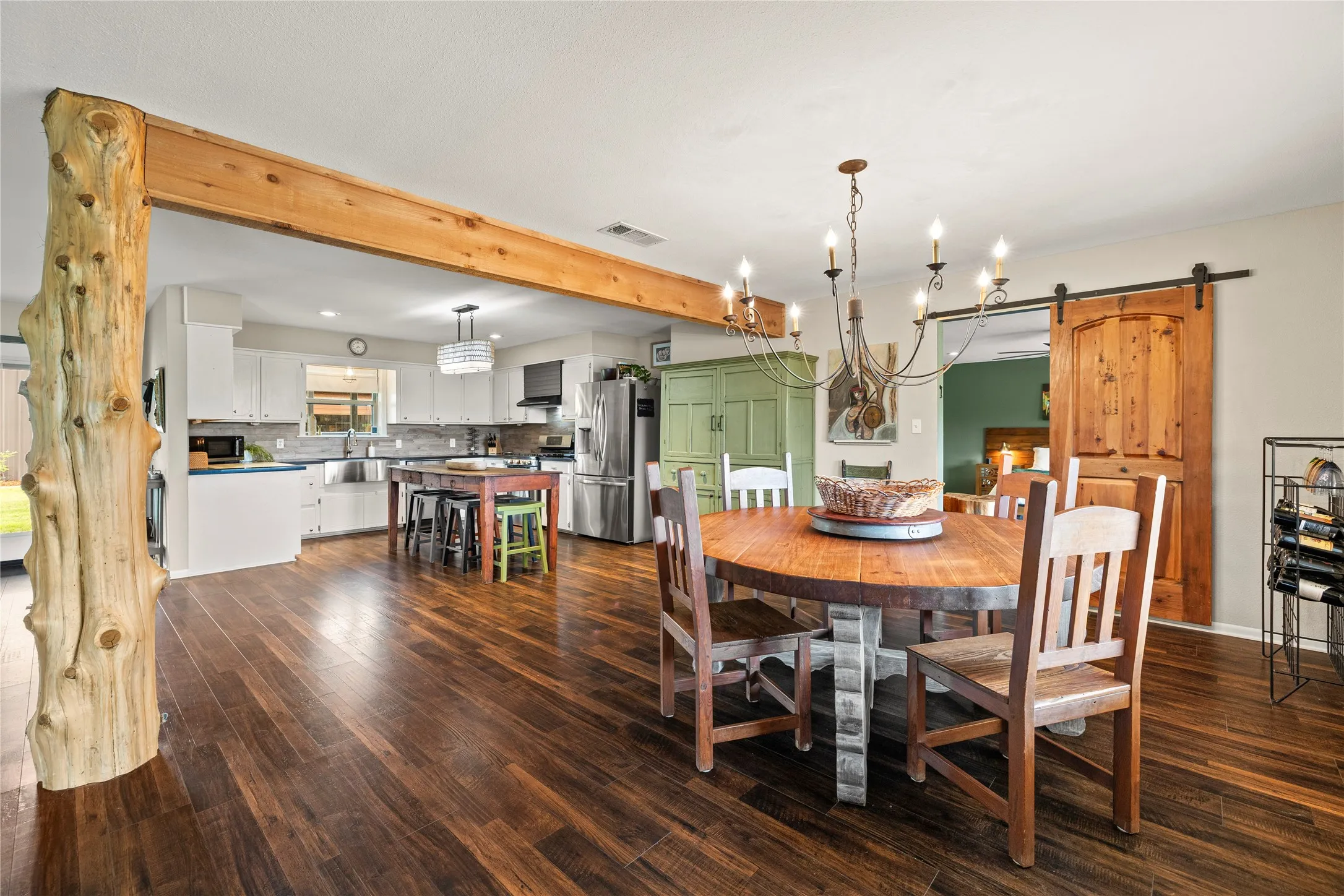 Open concept living space featuring wood-finish flooring, a wood beam, a tree trunk column, and a barn door