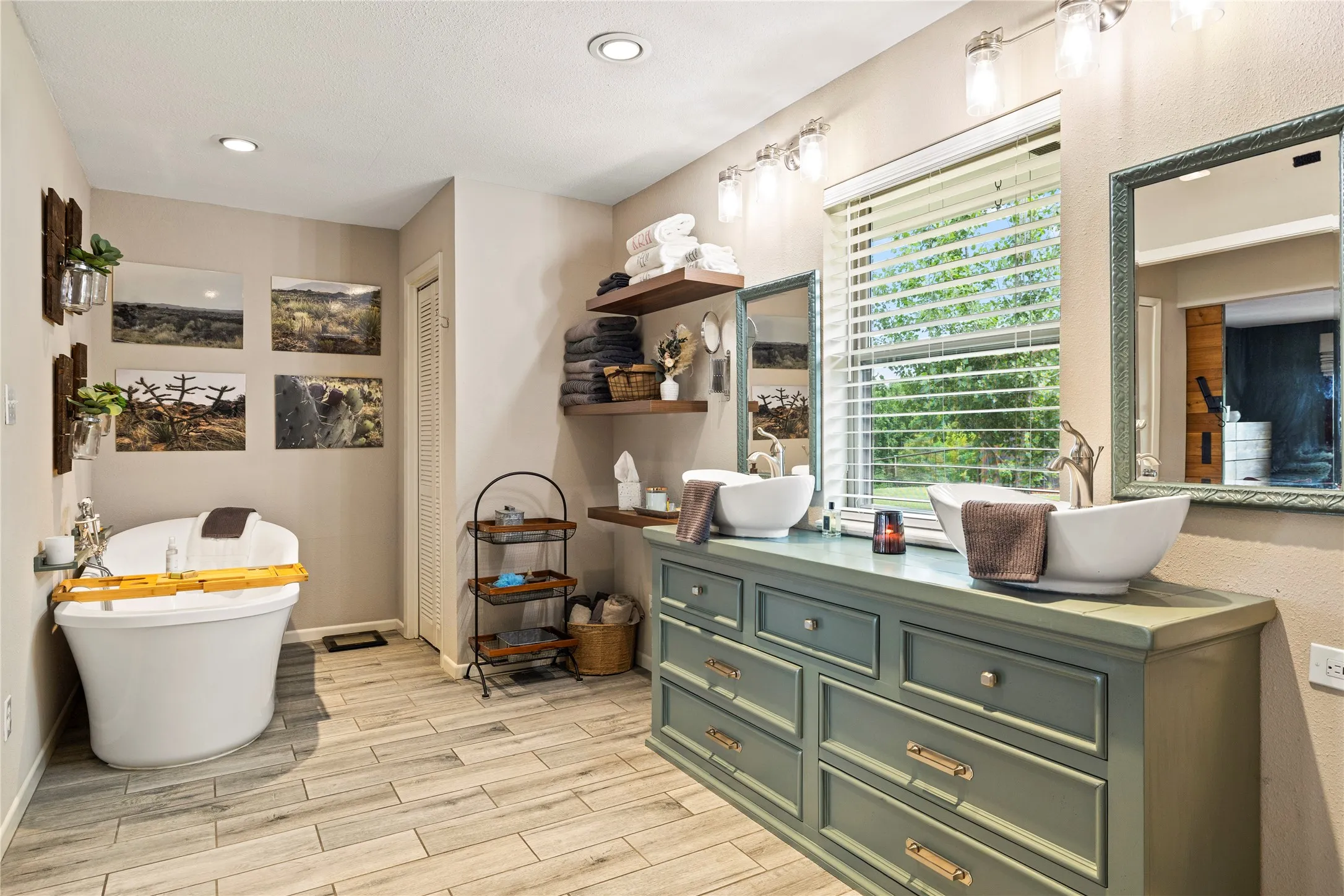 Spacious bathroom featuring a freestanding soaking tub, a dual vanity with vessel sinks, wood-finish flooring, and recessed lighting
