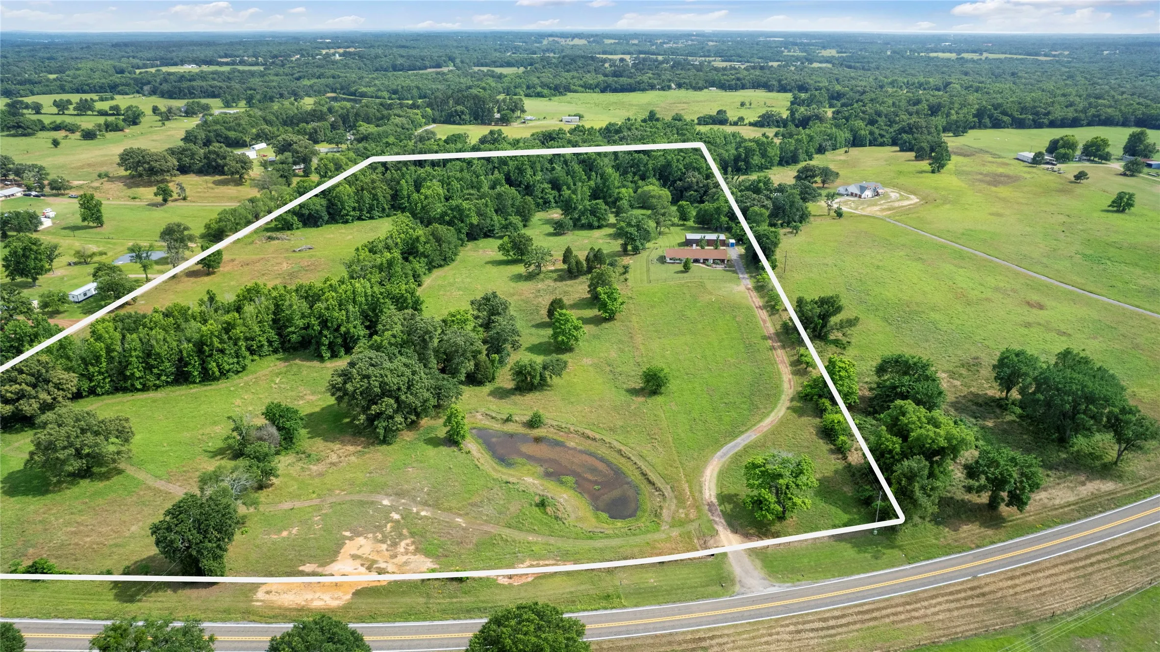 Expansive rural property featuring a single-story residence, a private pond, and mature tree lines