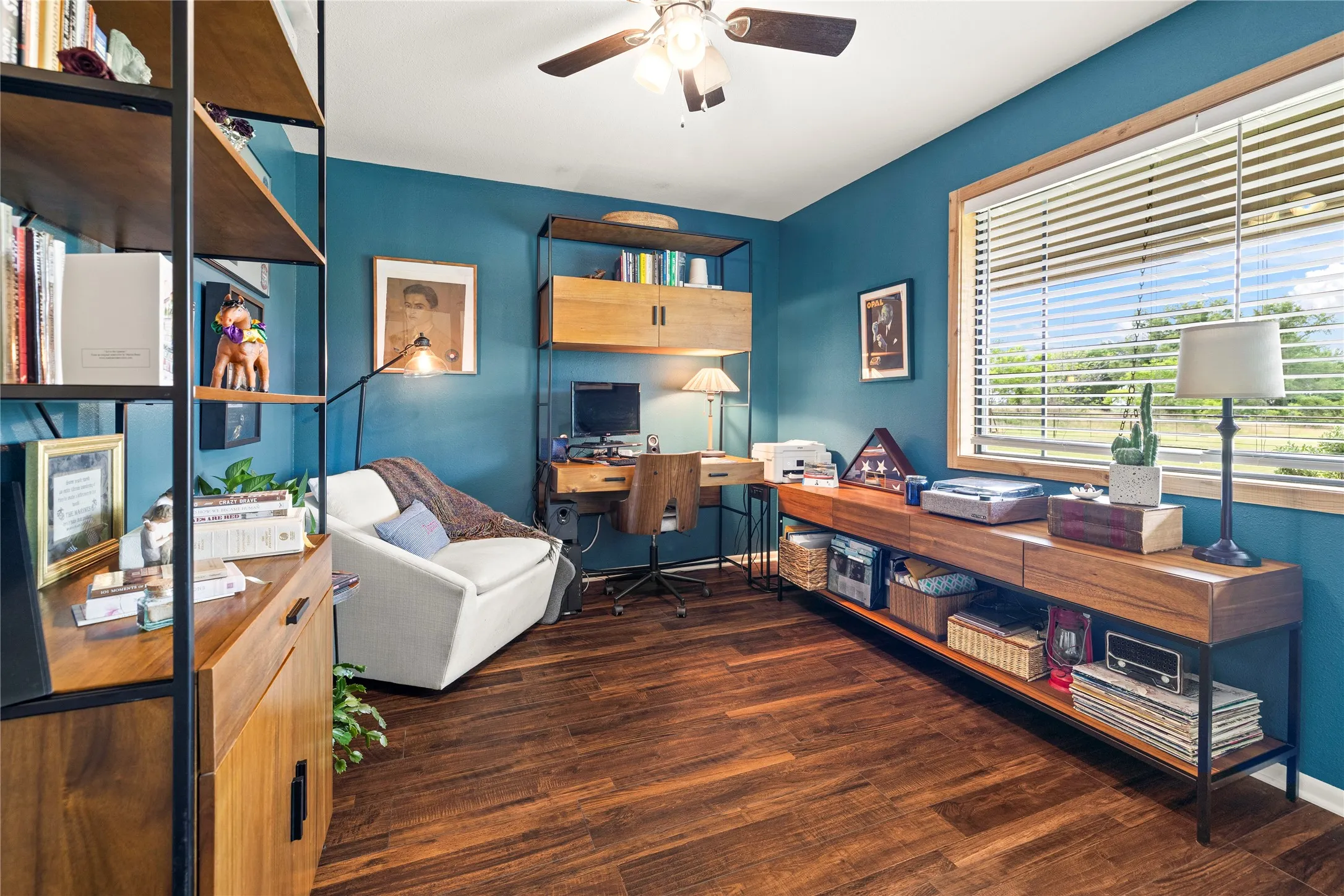 Interior space featuring wood-finish flooring, a ceiling fan with light fixture, and a large window with horizontal blinds