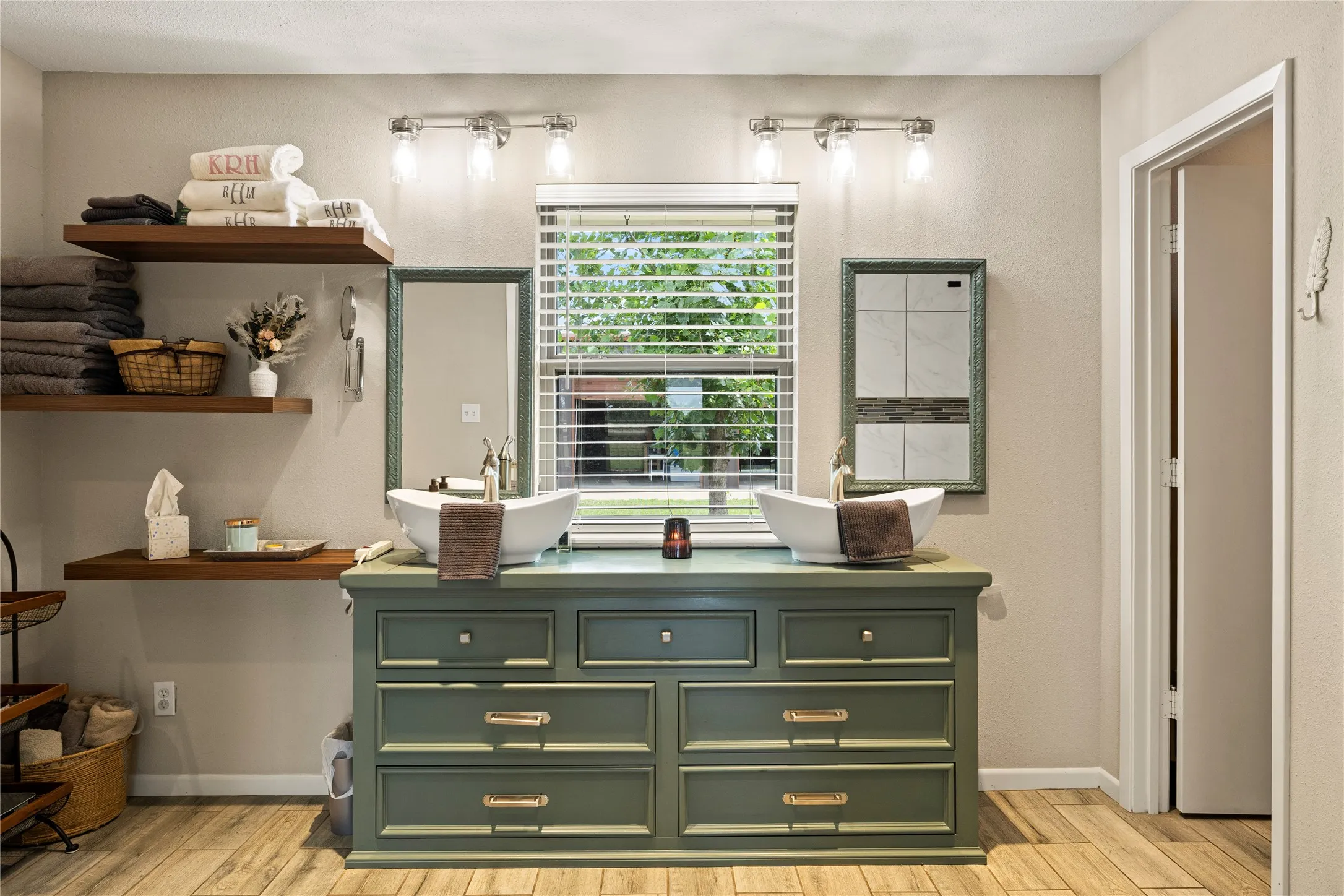 Bathroom featuring a double vanity with vessel sinks, wood-finish flooring, and floating wood shelves