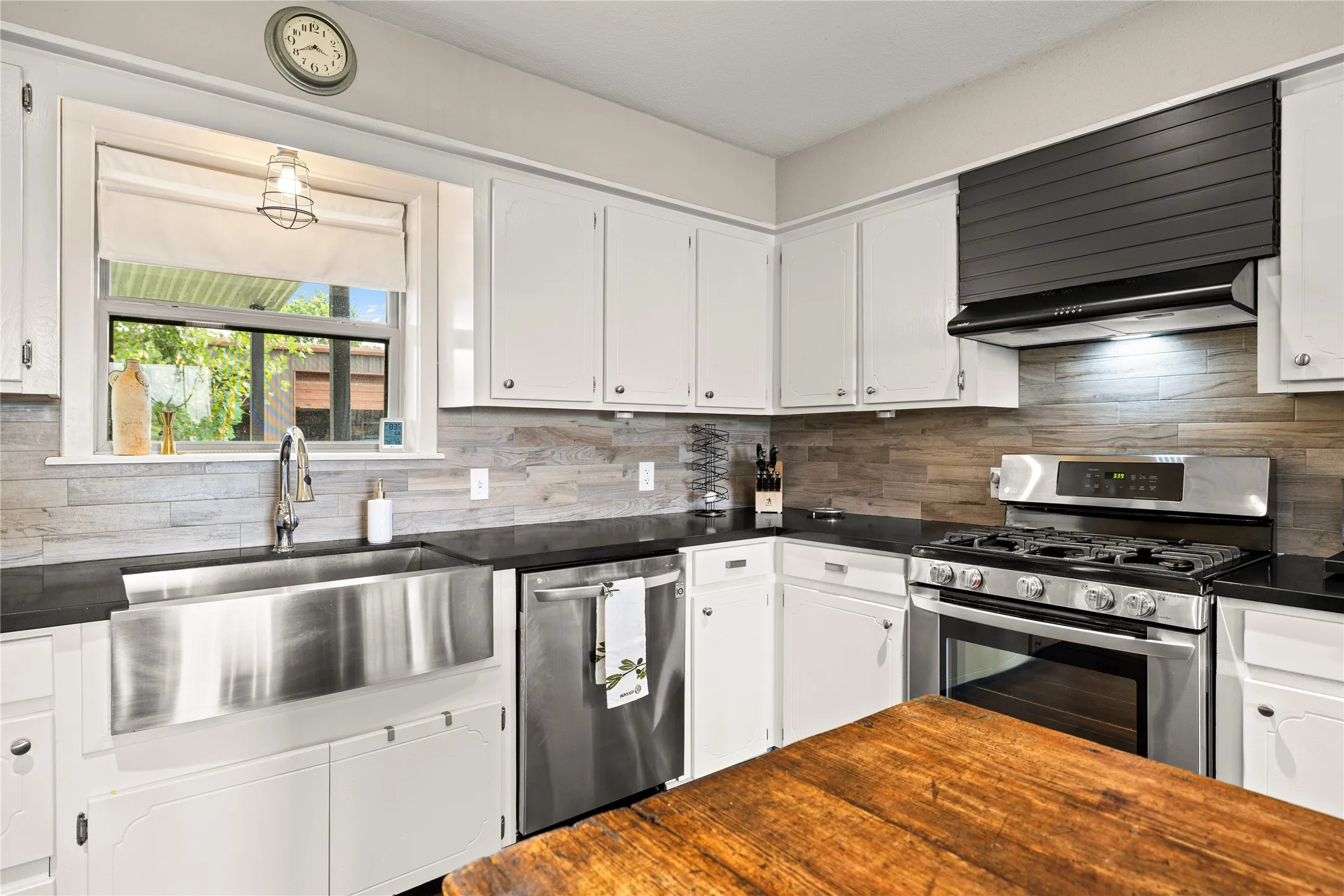 Kitchen featuring white cabinetry, black countertops, a stainless-steel farmhouse sink, a wood-finish backsplash, and stainless-steel appliances