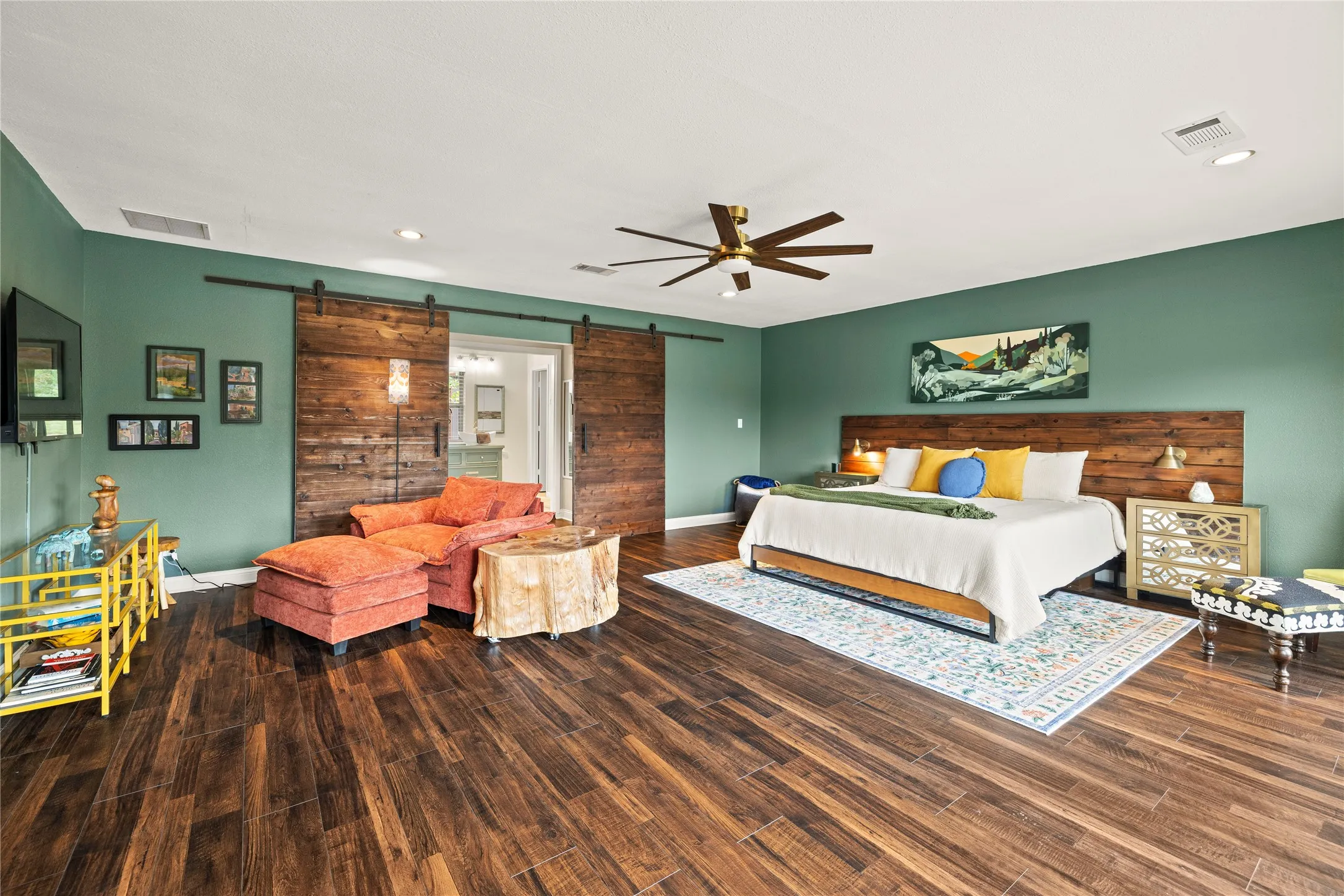 Spacious room featuring wood-finish flooring, a ceiling fan with integrated lighting, and a barn door entry