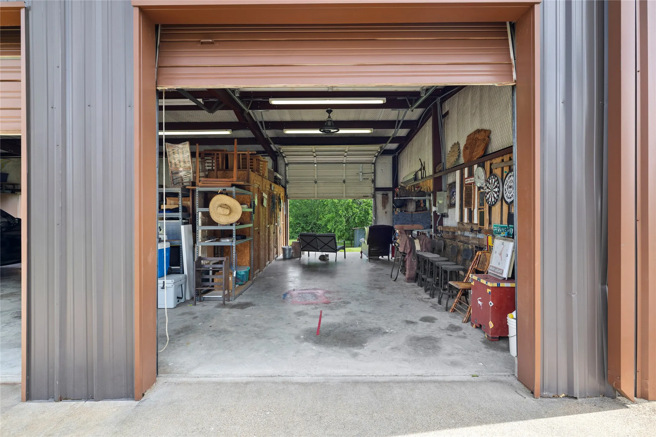 Spacious metal building featuring a large roll-up door, exposed steel beams, concrete flooring, and fluorescent lighting