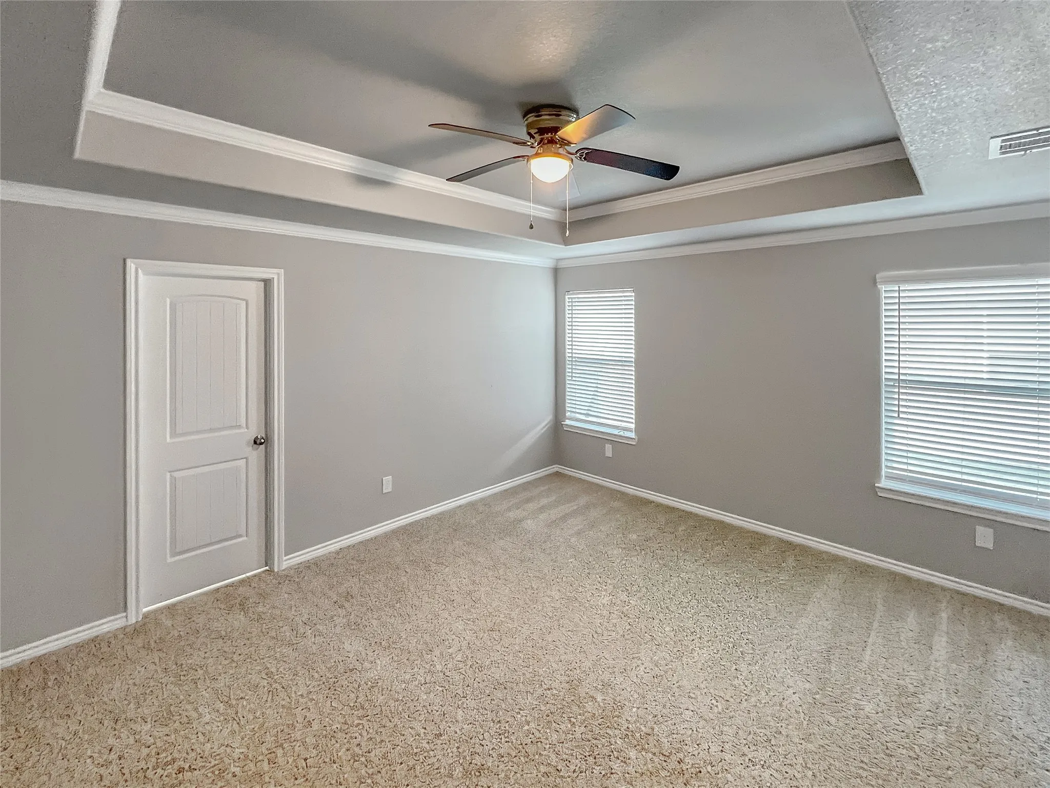 Recessed ceiling with crown molding and a ceiling fan, neutral carpet flooring, and two windows with blinds