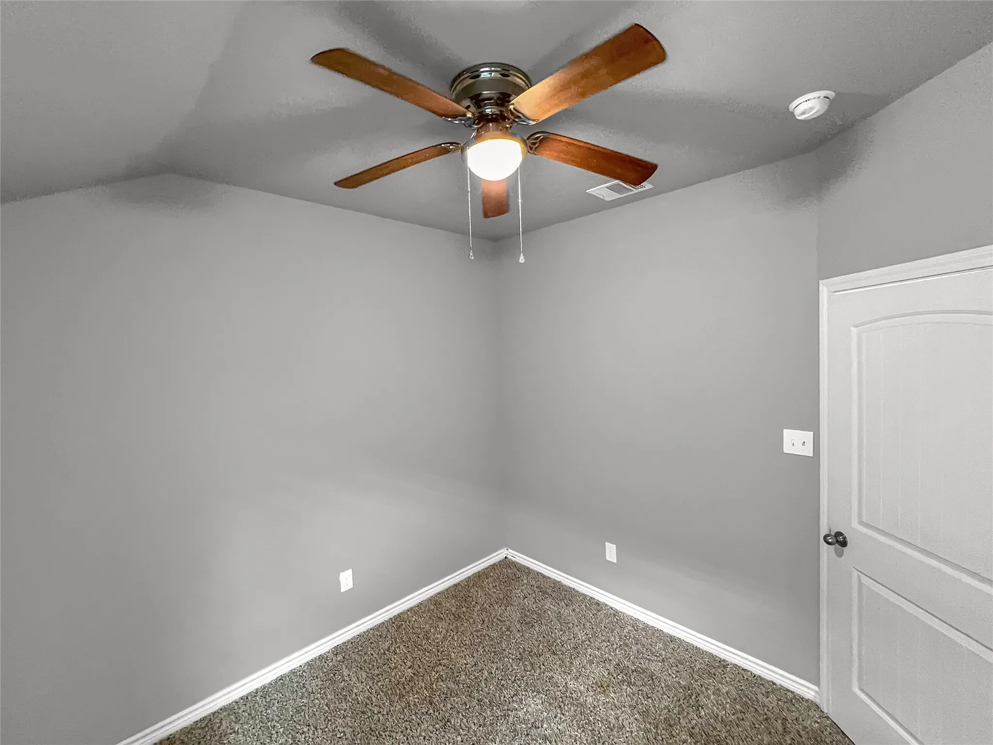 Room featuring a ceiling fan with wood-finish blades and integrated lighting, gray wall paint, and textured carpet flooring