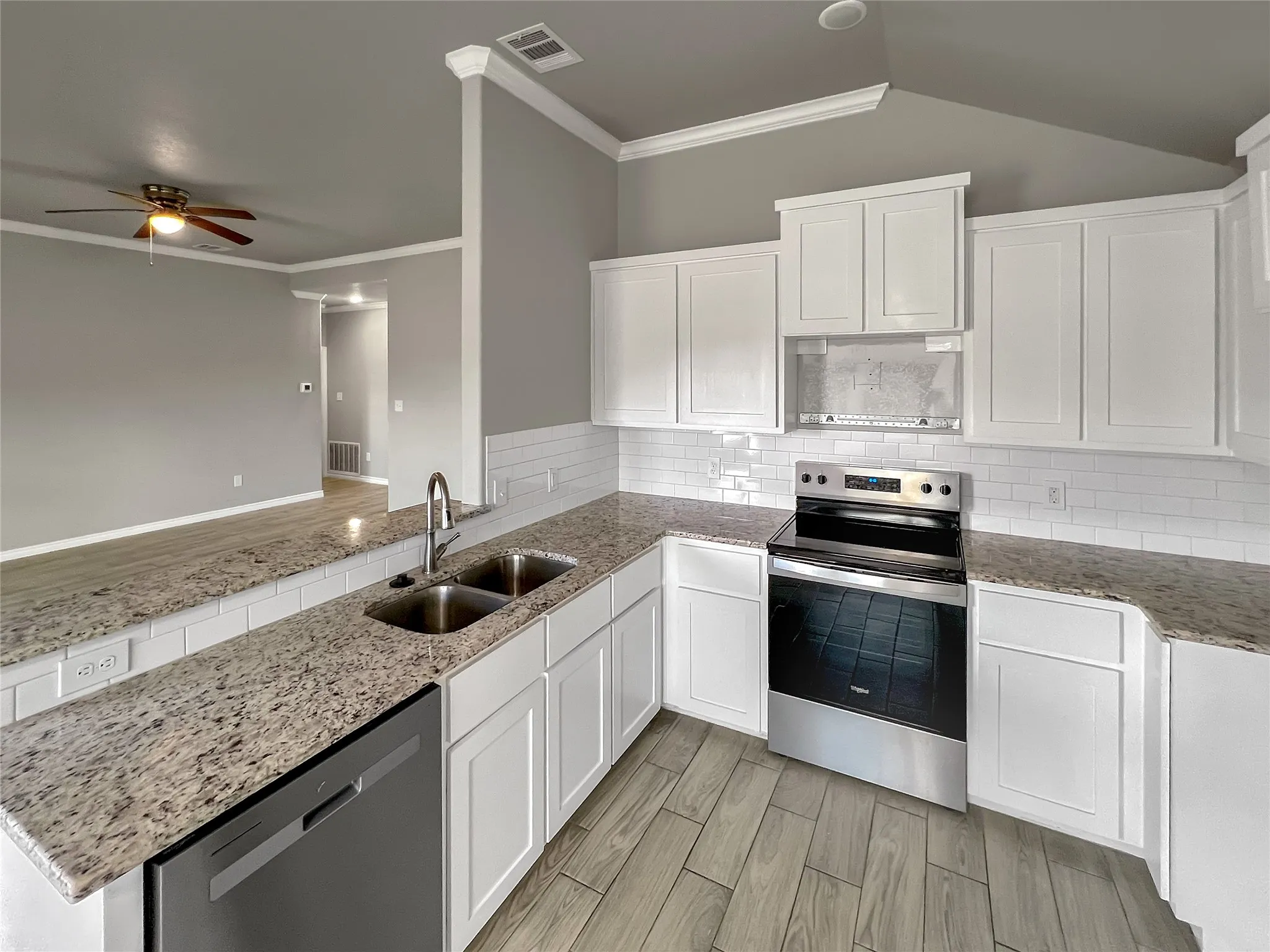 Modern kitchen featuring white shaker cabinetry, stainless steel appliances, granite-look countertops, subway tile backsplash, and wood-finish flooring