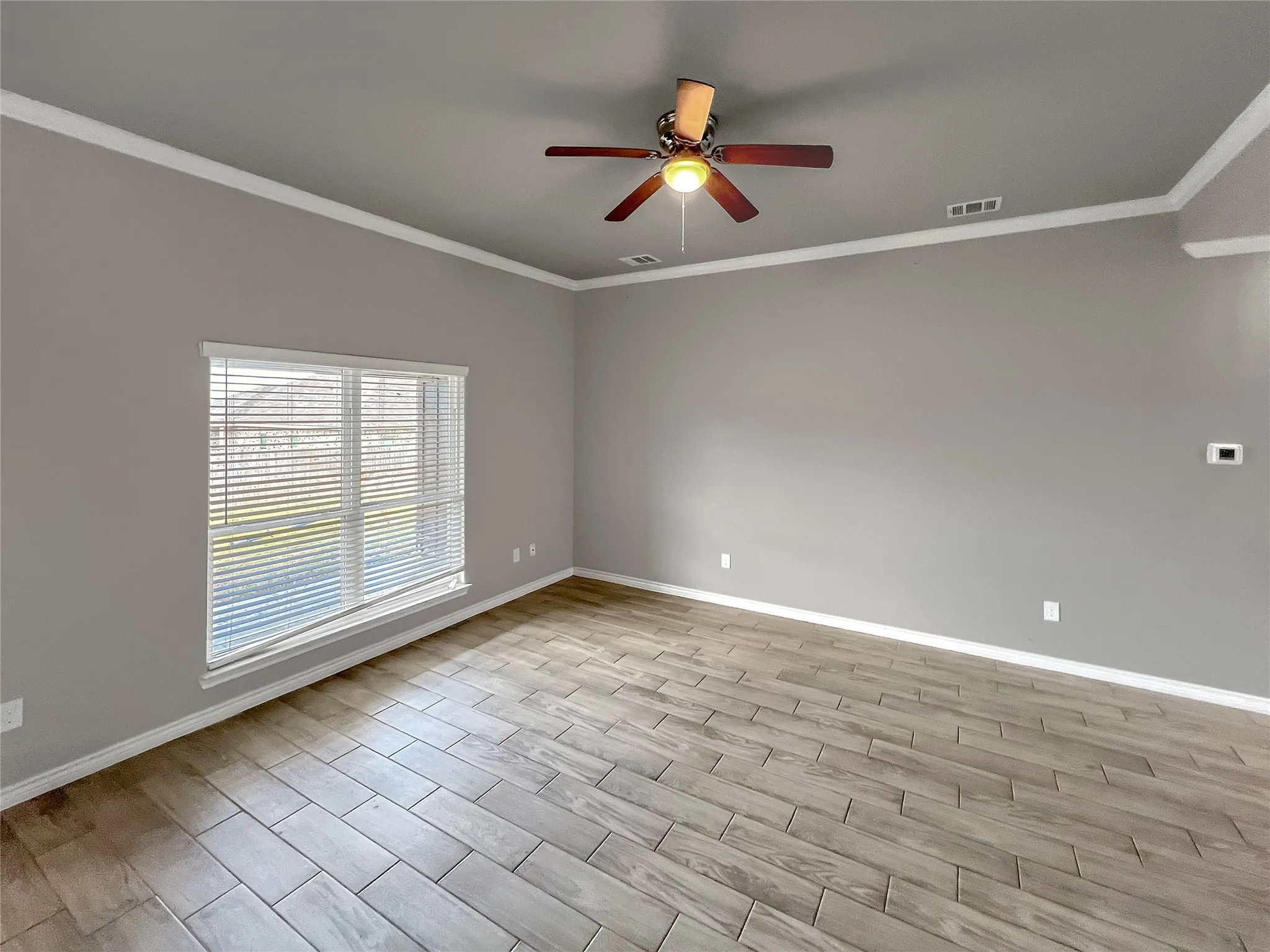 Spacious living area featuring a ceiling fan with integrated lighting, crown molding, and a large window with horizontal blinds