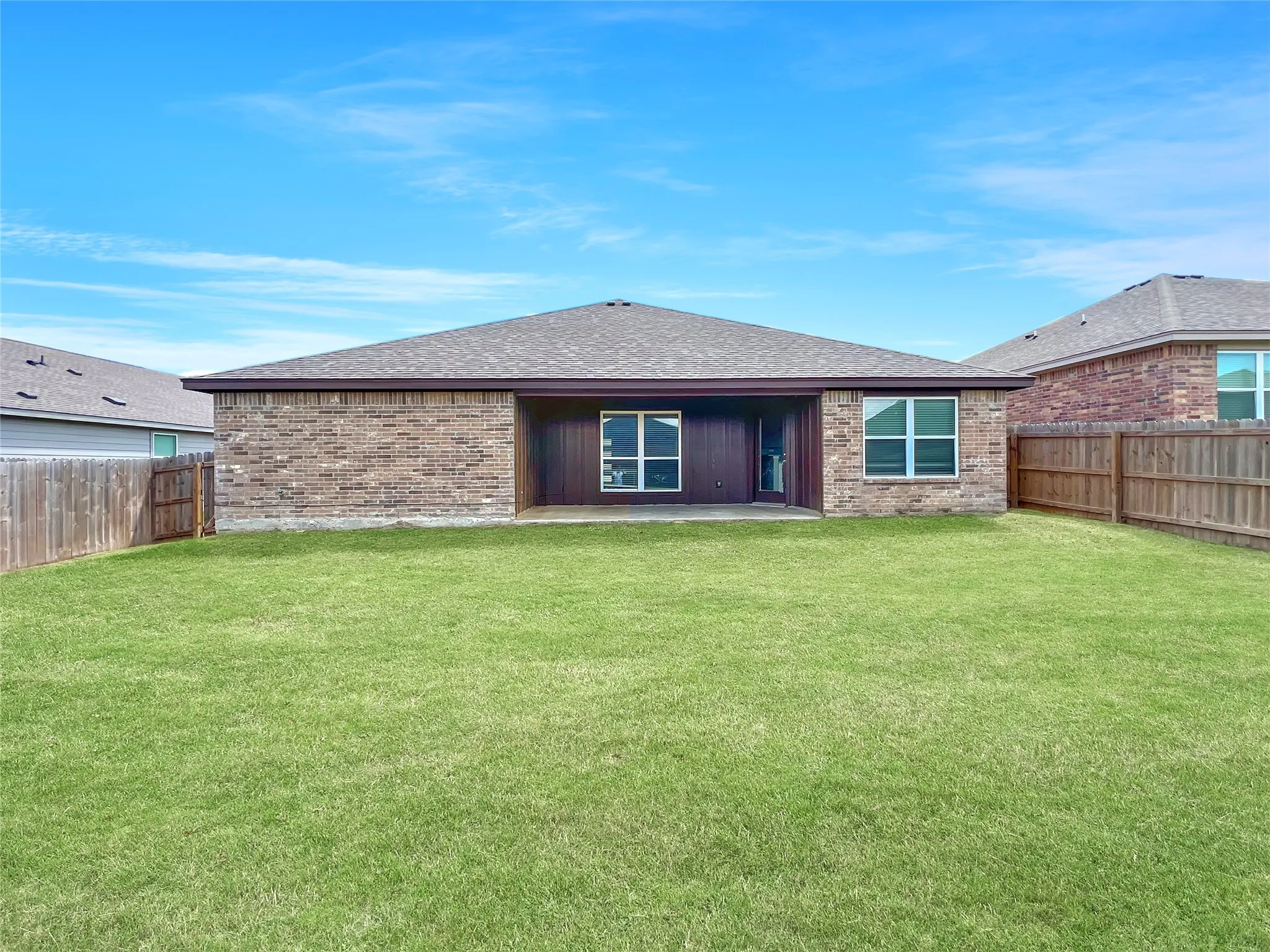 Expansive green lawn with a covered patio, brick exterior, and full privacy fencing