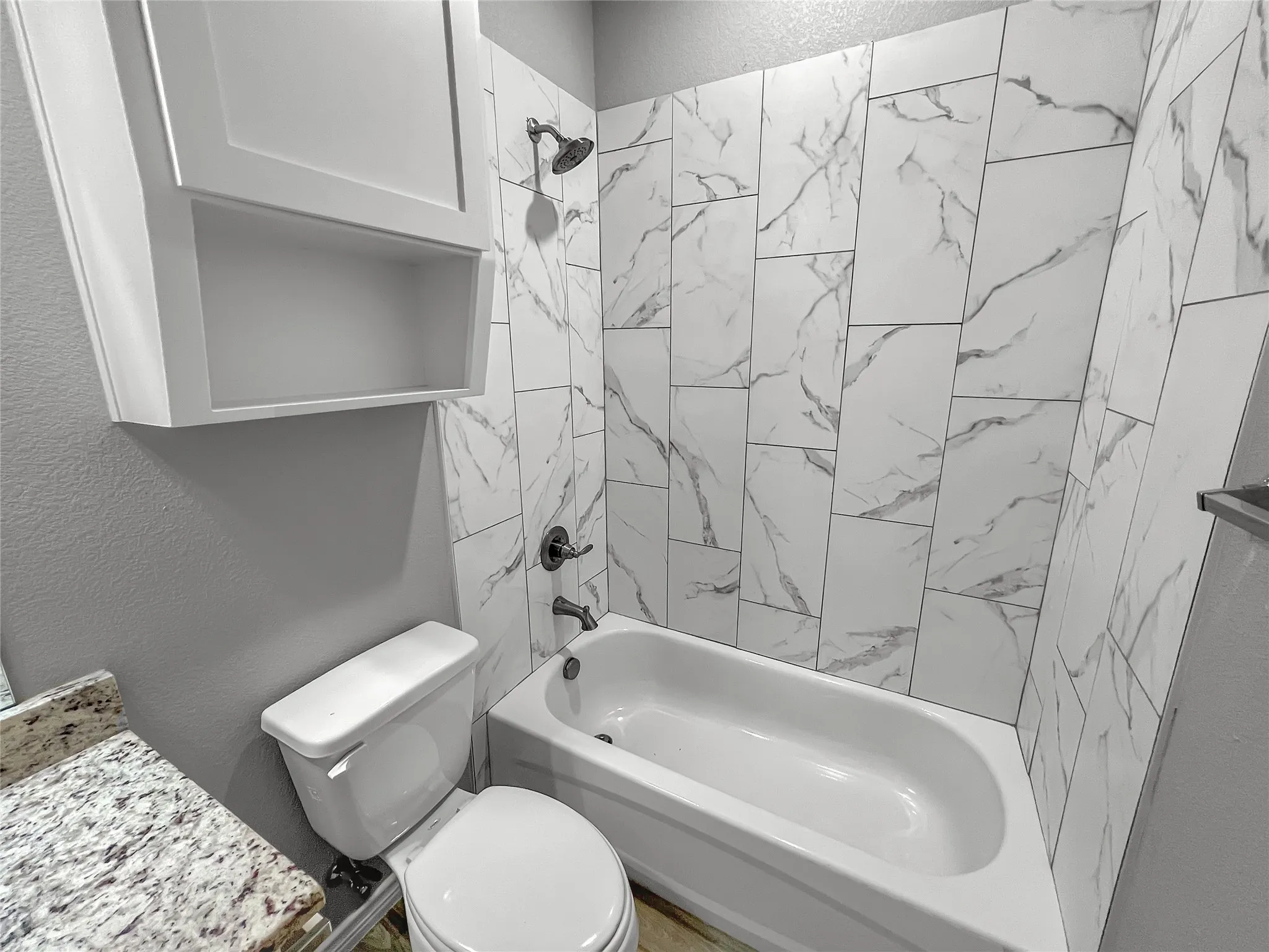 Bathroom featuring a white porcelain bathtub, wall-mounted showerhead, and tiled surround with a marble-look pattern