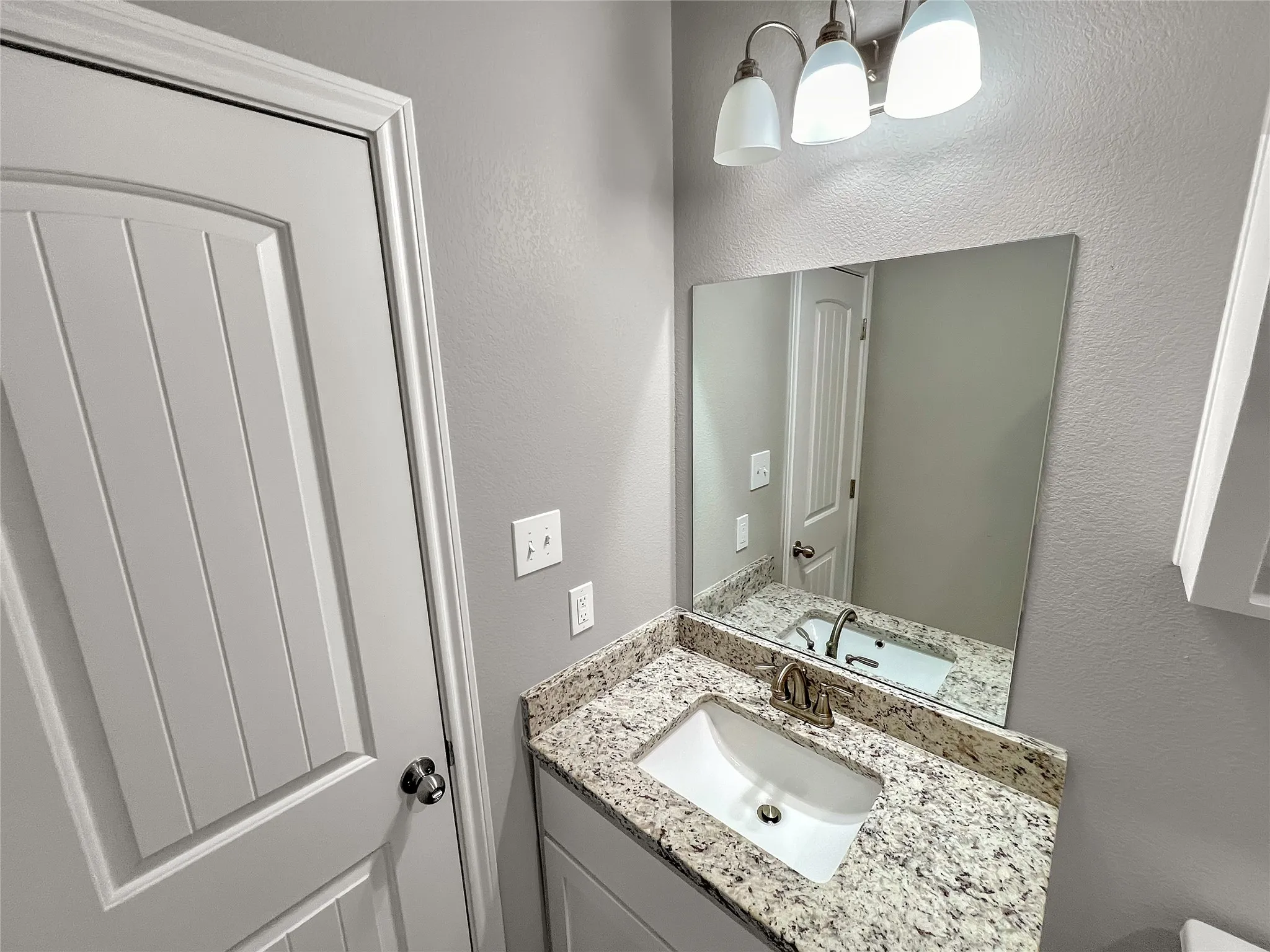 Bathroom vanity featuring a granite-finish countertop, under-mount sink, and brushed nickel faucet