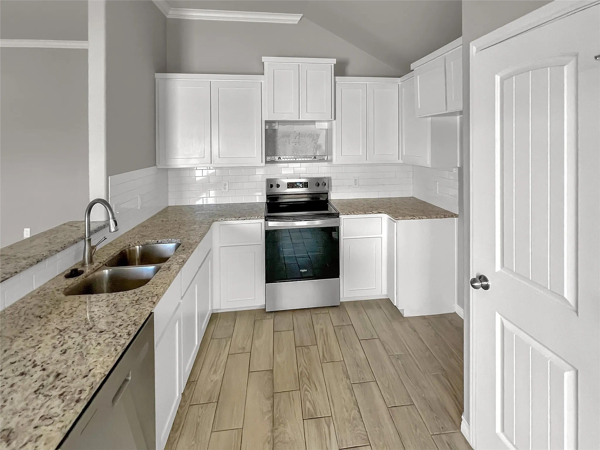 Kitchen featuring white cabinetry, granite countertops, stainless steel appliances, a subway tile backsplash, and wood-finish flooring