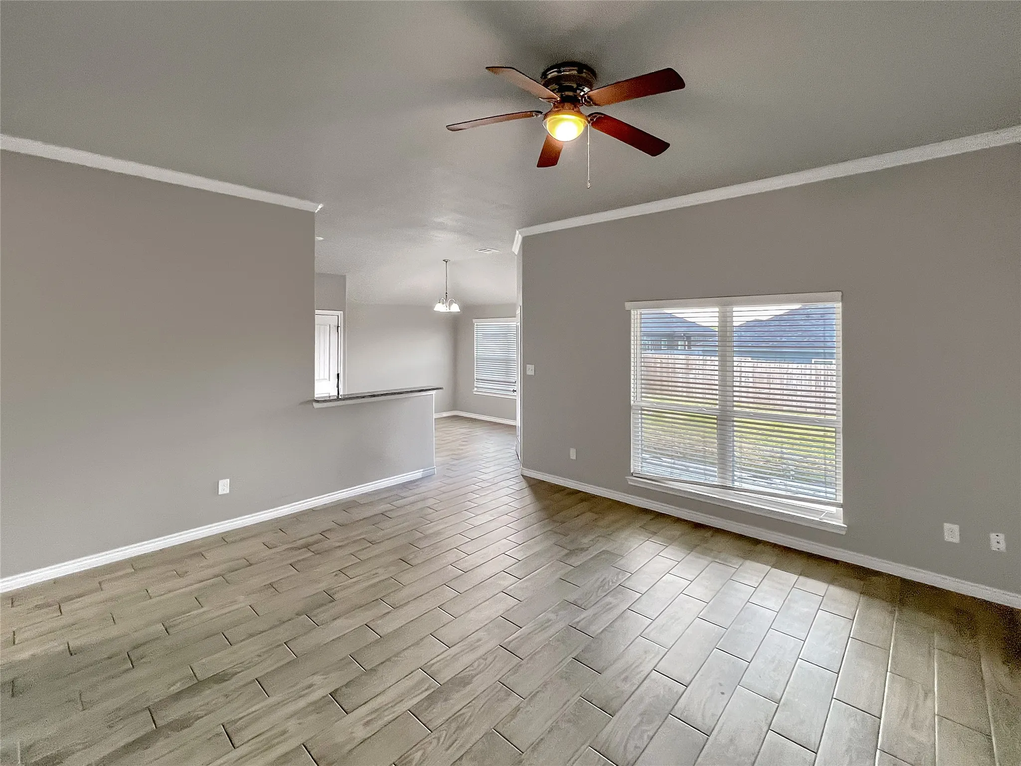 Spacious room featuring wood-look tile flooring, a ceiling fan with integrated lighting, and a large window