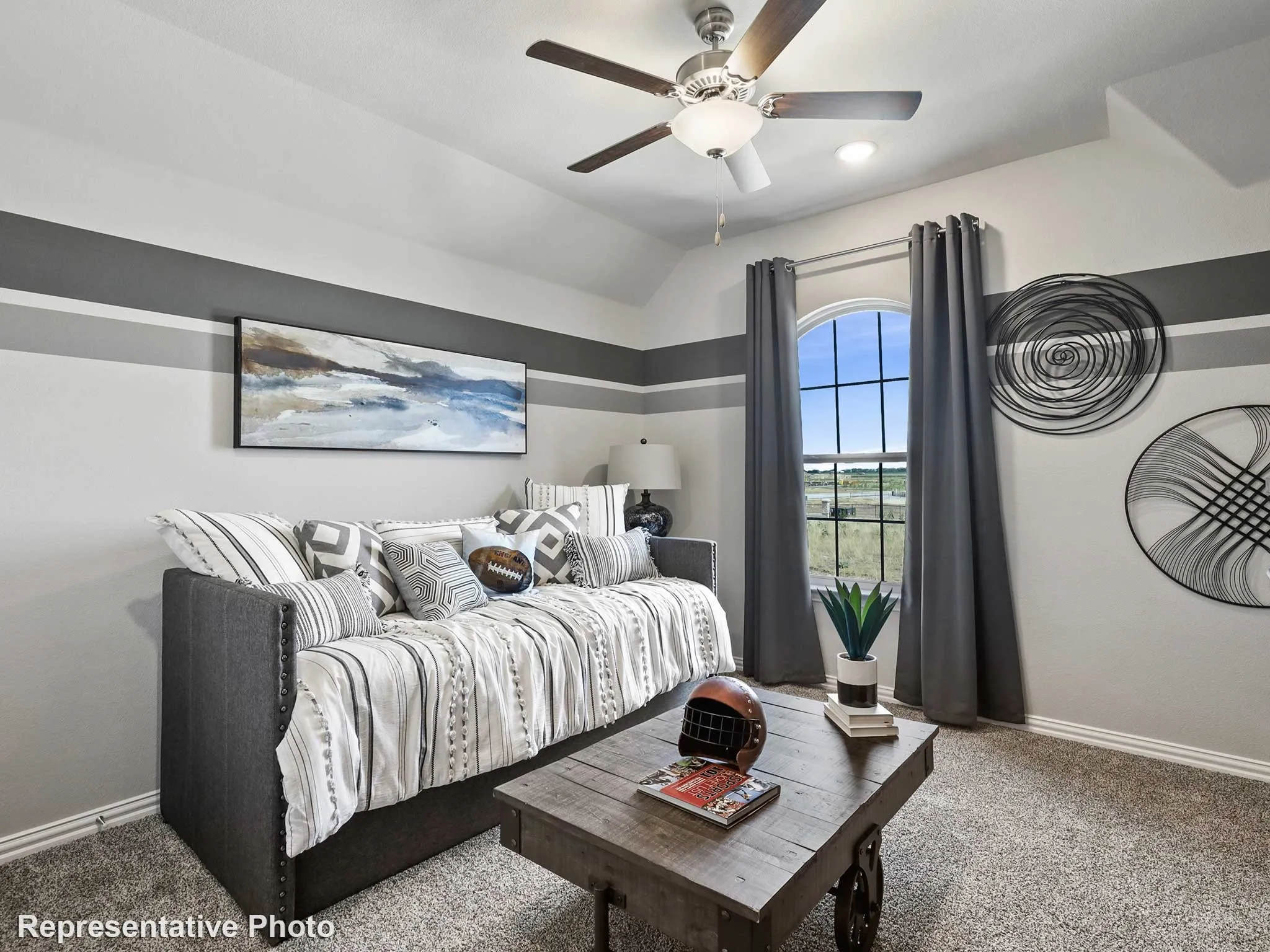 Carpeted room featuring a vaulted ceiling with a ceiling fan, accent wall with horizontal stripes, and an arched window