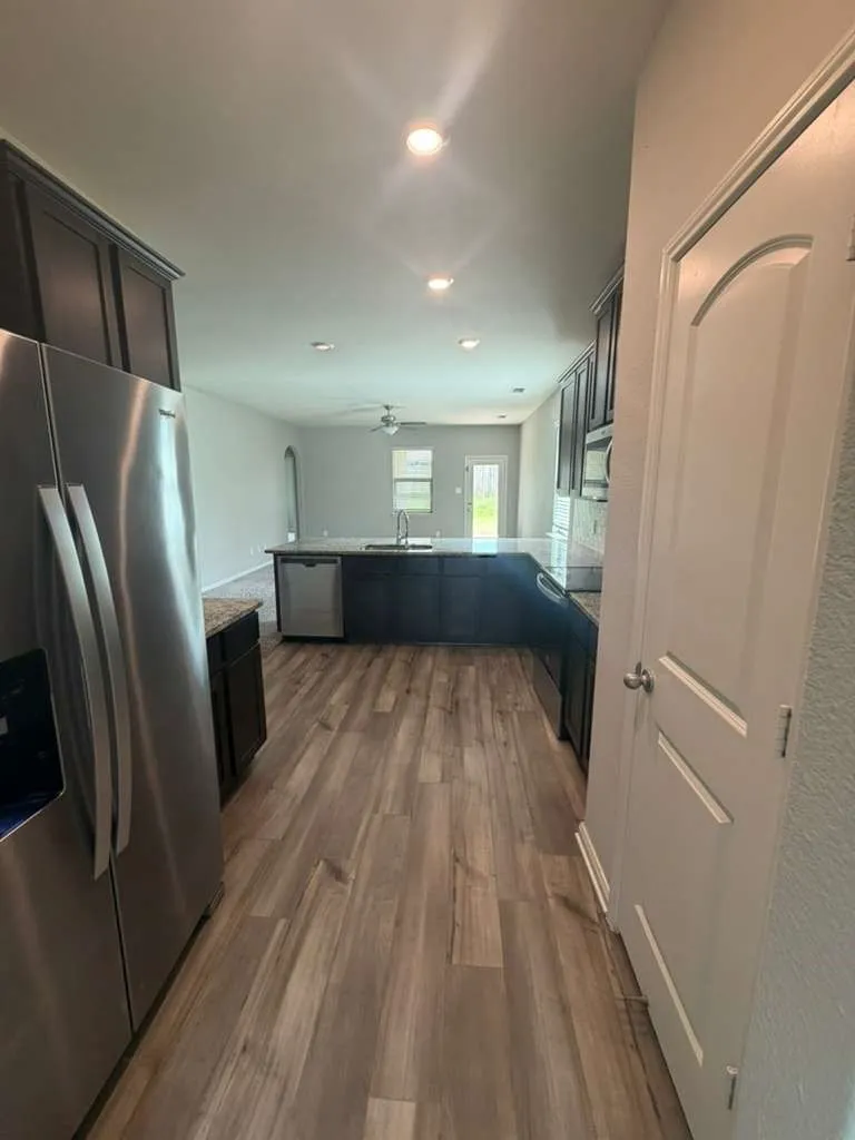 Open-concept kitchen featuring wood-finish flooring, dark wood cabinetry, stainless steel appliances, and recessed lighting
