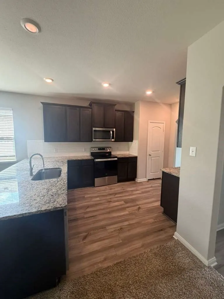 Kitchen featuring dark wood-finish cabinetry, granite-style countertops, stainless steel appliances, and a subway tile backsplash