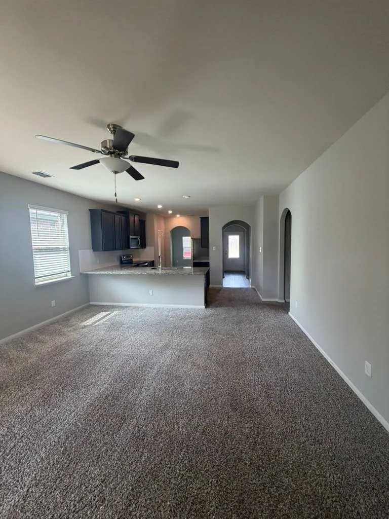 Open-concept living area featuring a ceiling fan, plush carpet, and a kitchen with dark cabinetry, light countertops, and recessed lighting