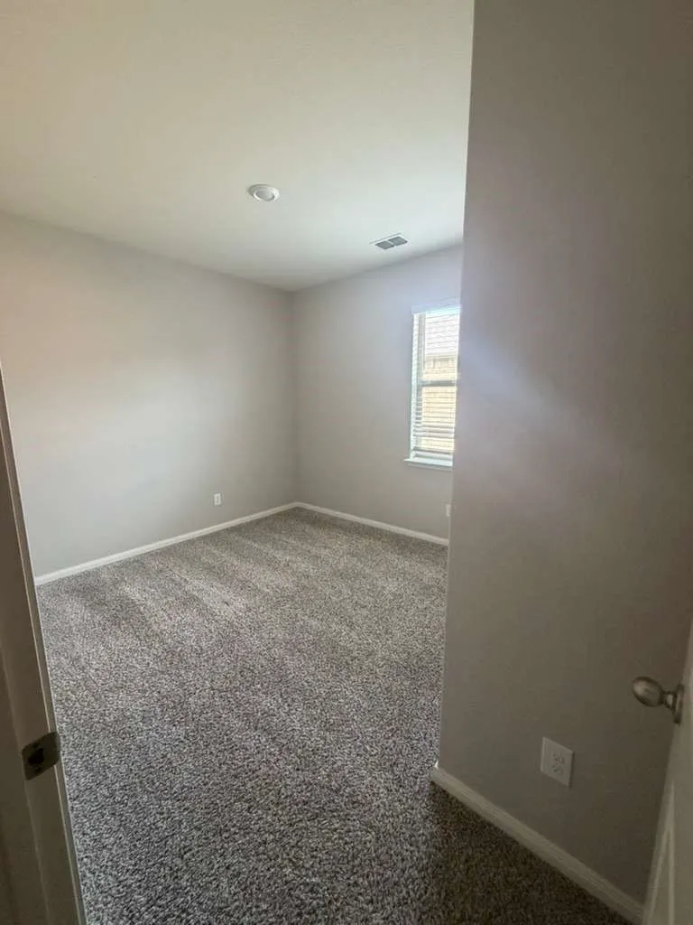 Spacious room featuring neutral carpeting, light-colored walls, and a window with horizontal blinds