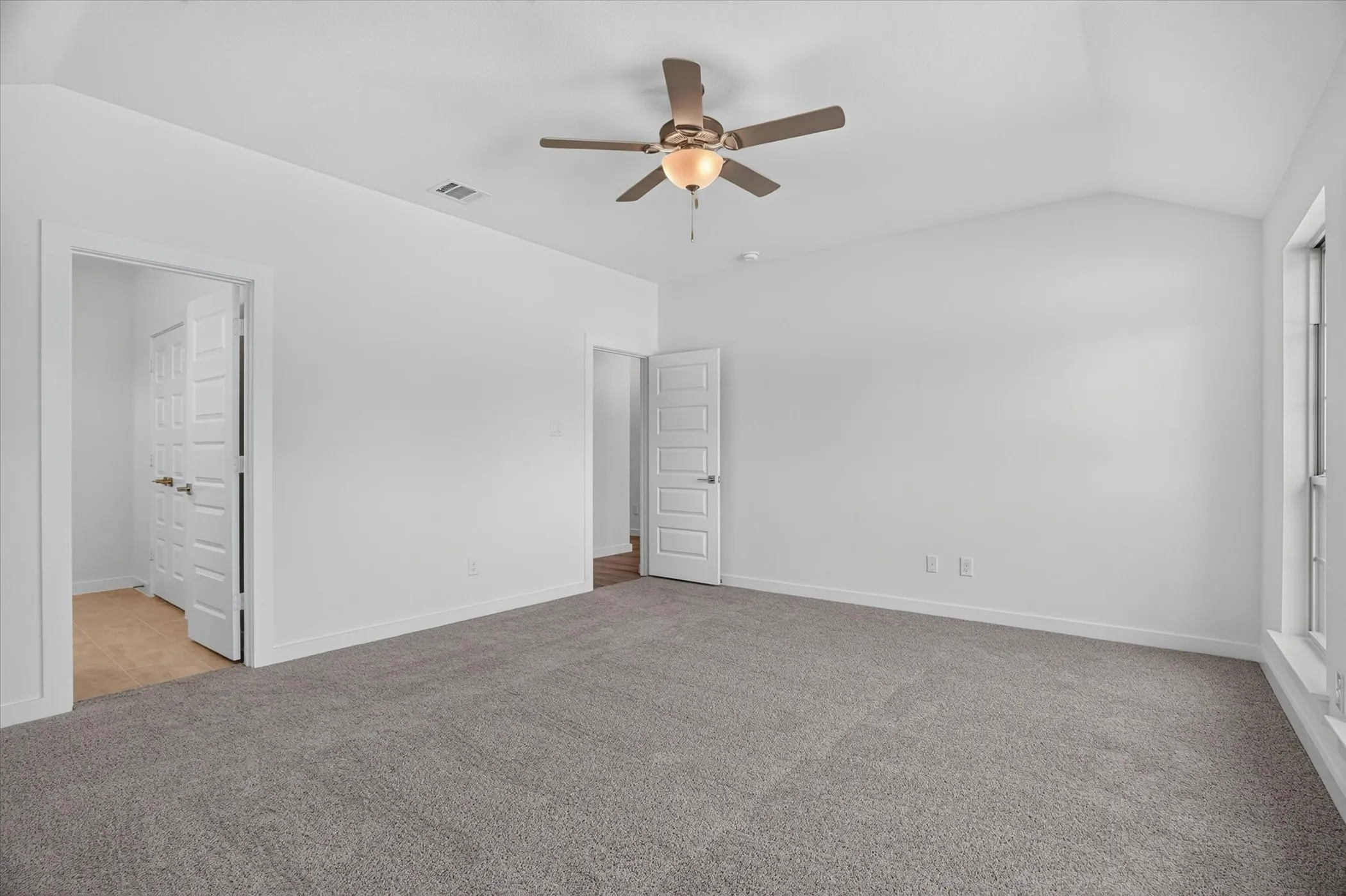 Spacious room featuring vaulted ceilings, a ceiling fan with integrated lighting, neutral gray carpeting, white walls, and white trim
