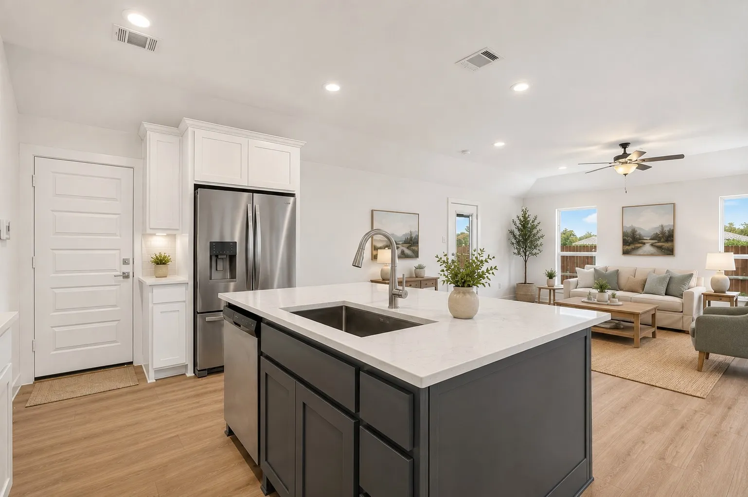 Open-concept living area featuring a kitchen island with a built-in sink, white cabinetry, stainless steel appliances, wood-finish flooring, and multiple windows providing natural light