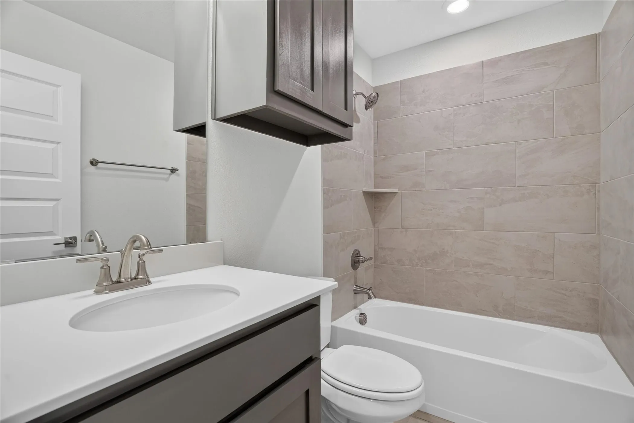 Bathroom featuring a white bathtub, tiled shower surround, recessed shower niche, and a vanity with a white countertop and wood-finish cabinetry