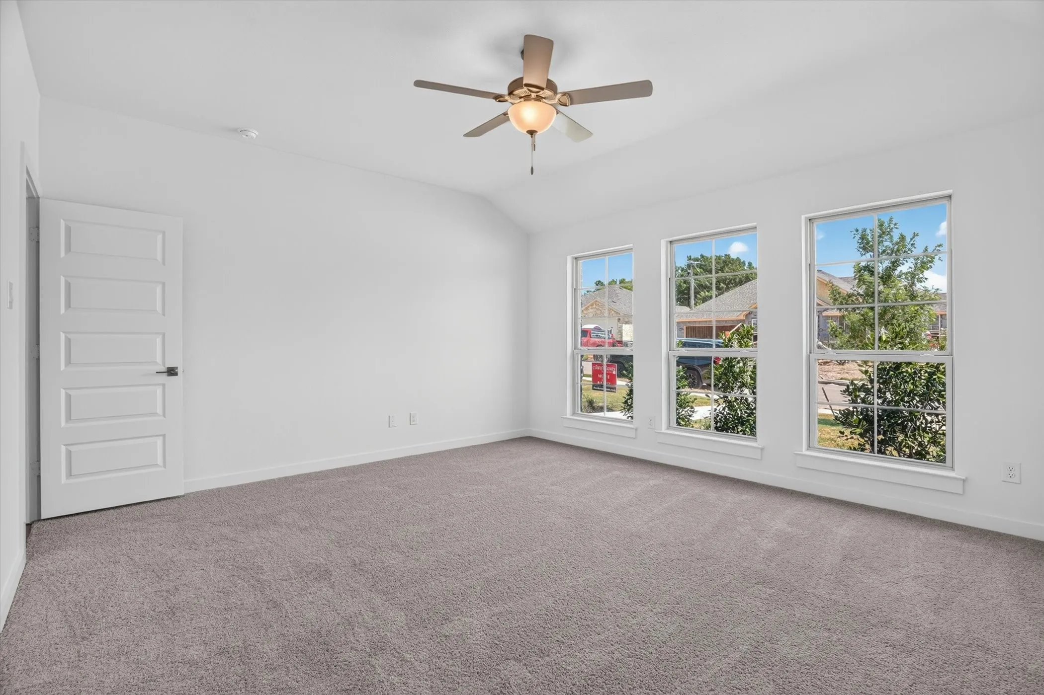 Spacious room featuring three large windows, vaulted ceiling, and neutral-toned carpeting