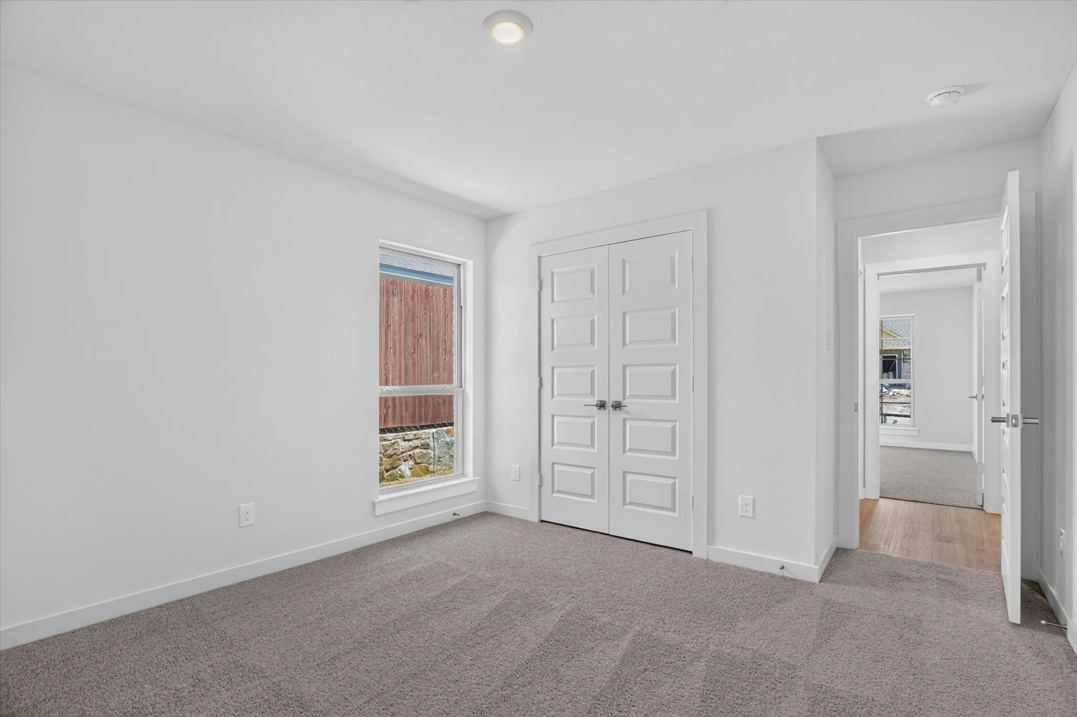 Spacious bedroom featuring neutral wall finishes, carpet flooring, and abundant natural light from a large window