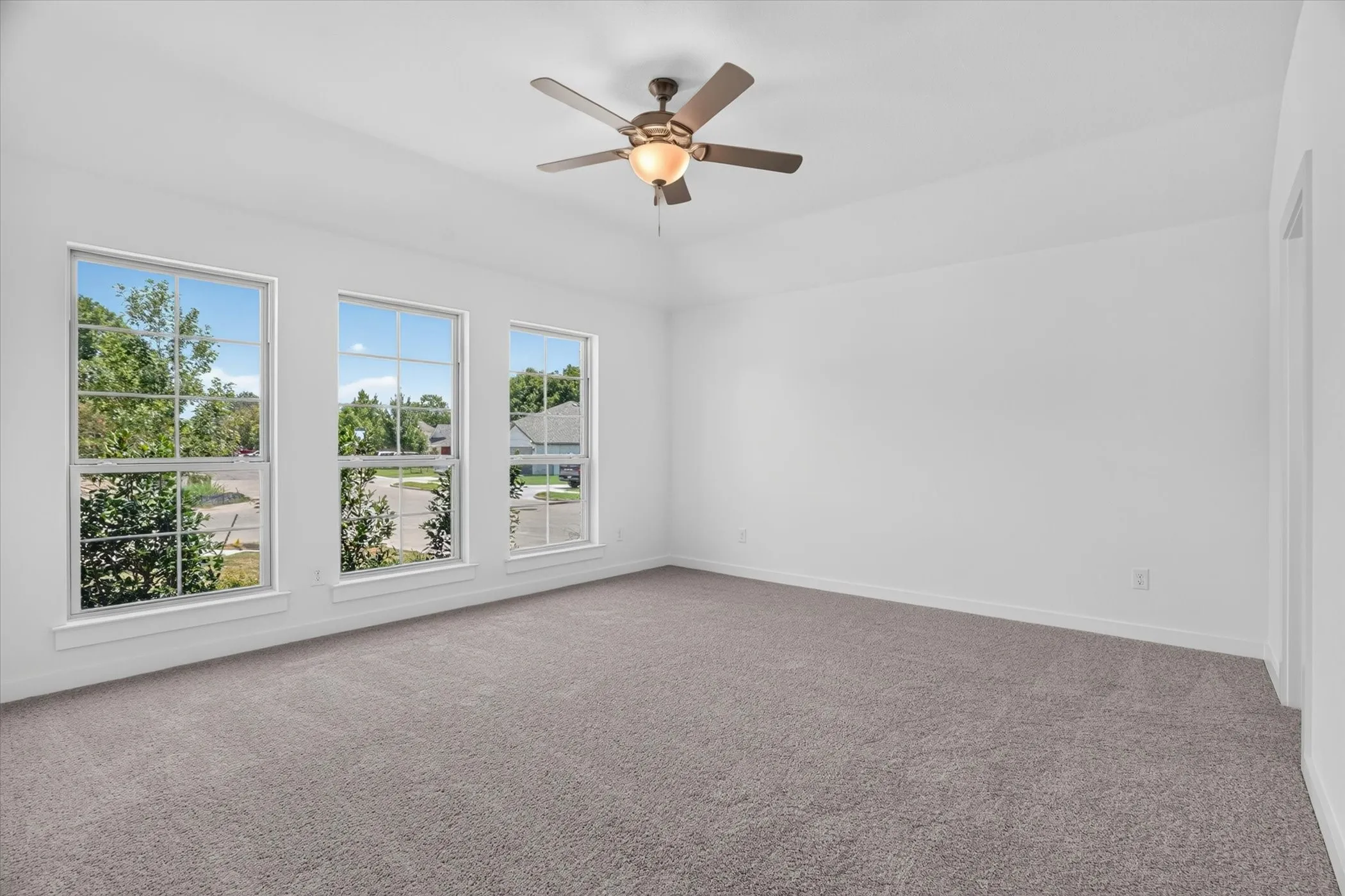 Spacious room featuring three large windows, white walls, and gray carpeting