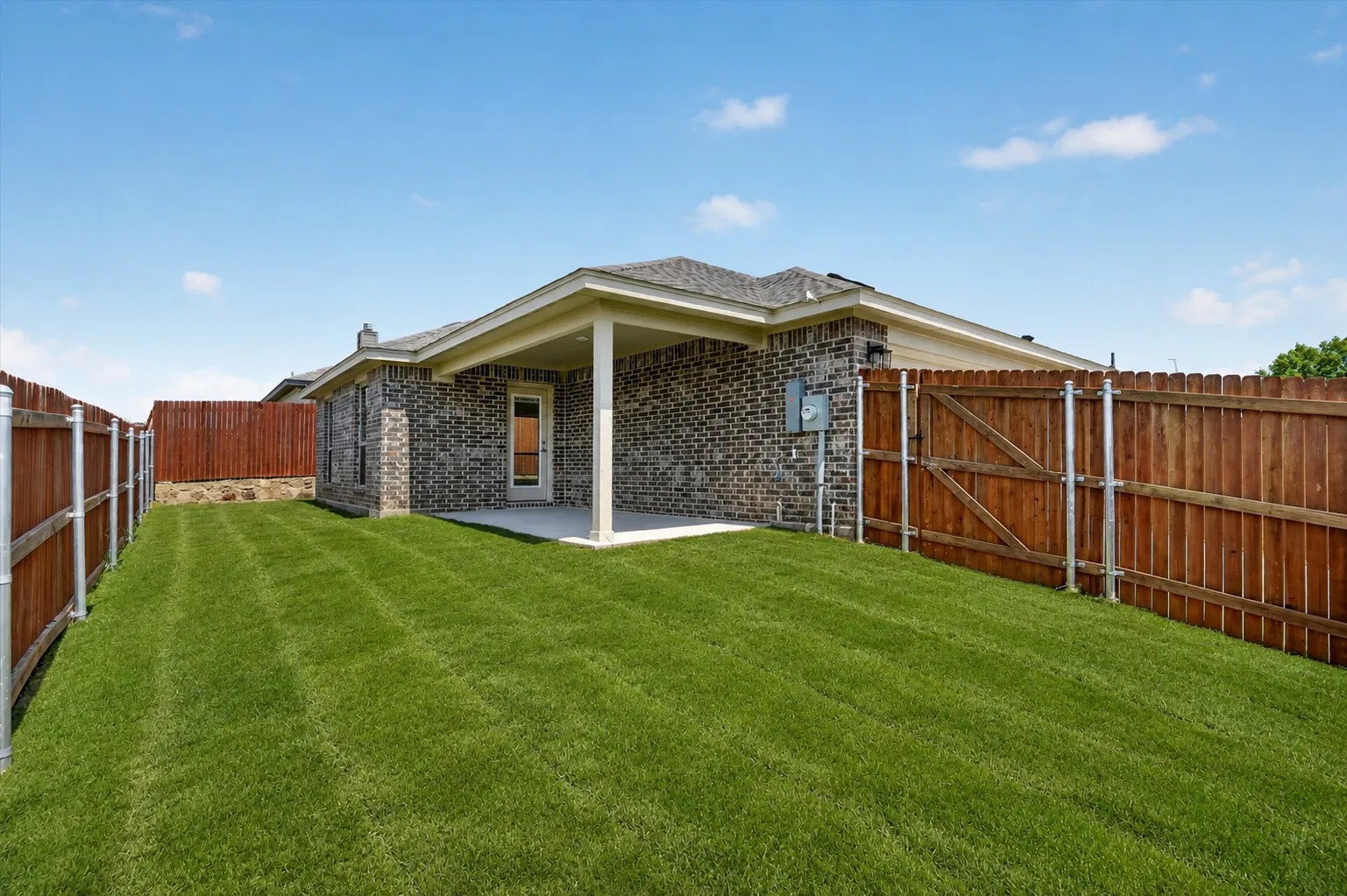 Expansive backyard featuring a manicured lawn, full privacy fencing, and a covered concrete patio
