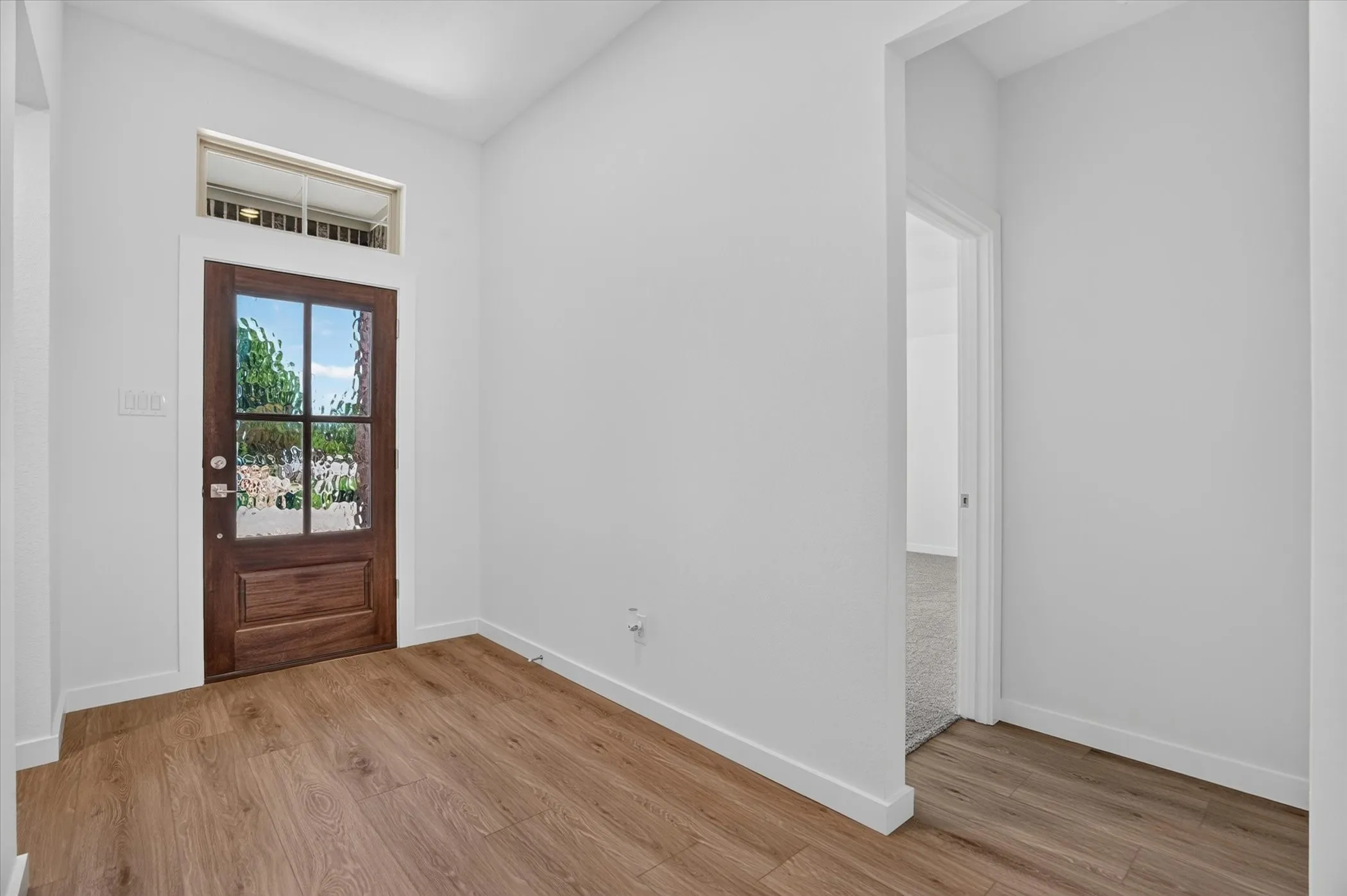 Bright foyer featuring hardwood flooring, clean white walls, and abundant natural light from the transom-topped entry door with glass panels