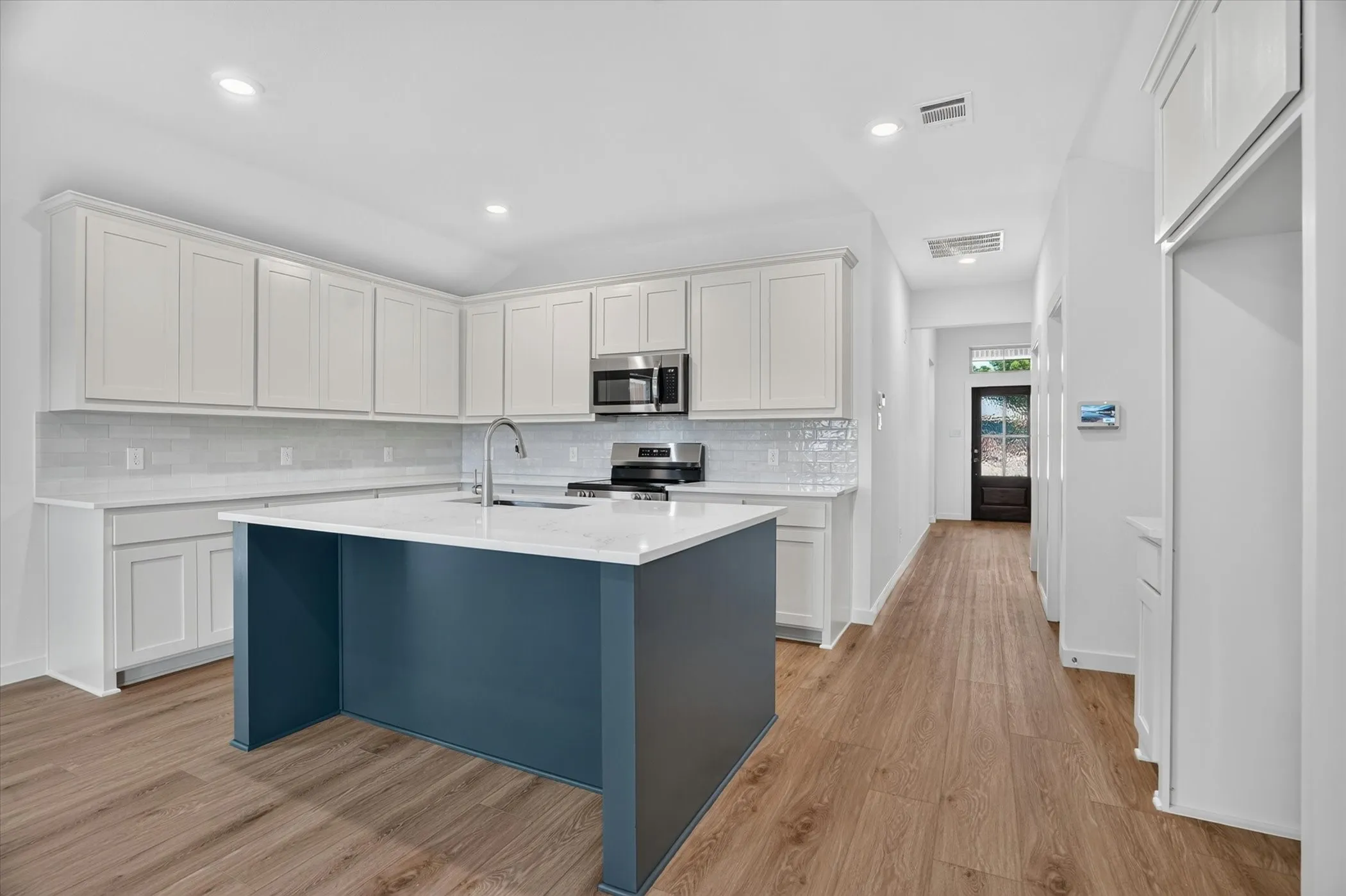 Modern kitchen featuring white shaker-style cabinetry, stainless steel appliances, subway tile backsplash, quartz countertops, and a striking navy blue island with waterfall edge detail