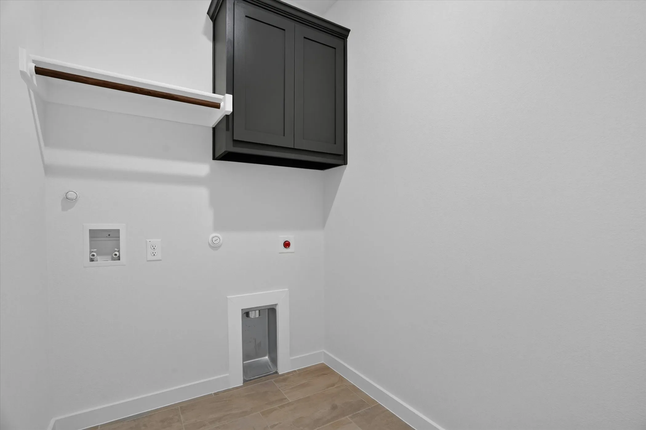 Utility room featuring light-toned tile flooring, a dark-toned upper storage cabinet, a wall-mounted drying rack with a wood-finish rod, and baseboard molding