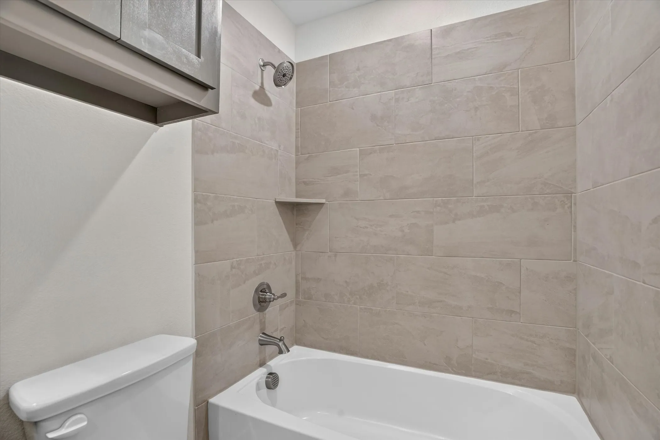 Updated bathroom featuring tile surround walls, a white porcelain soaking tub with chrome fixtures, and a recessed shelf niche for storage