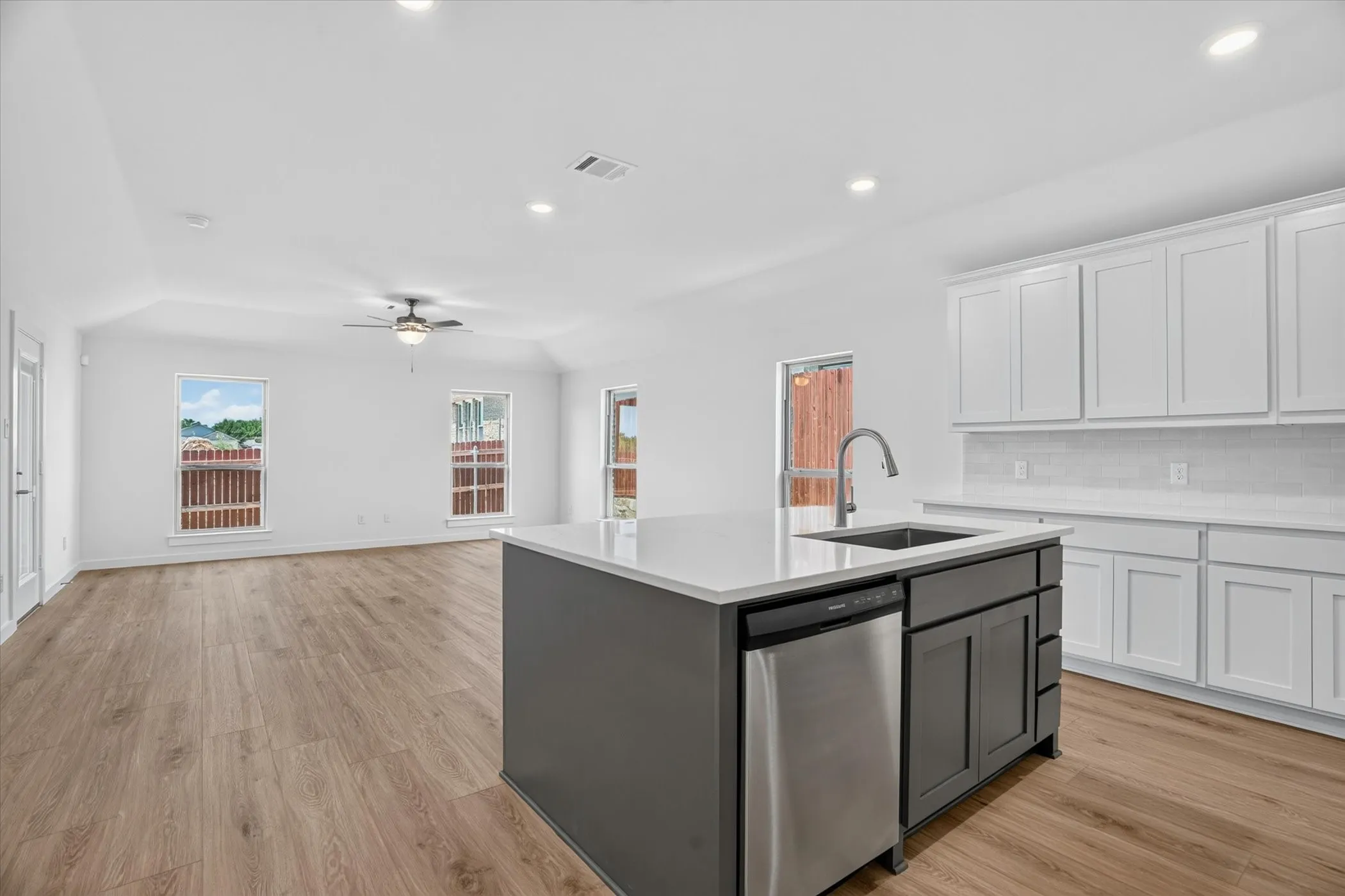 Open-concept kitchen and living area featuring white shaker-style cabinetry, a black kitchen island with stainless steel appliances, quartz countertops, and an undermount sink with gooseneck faucet