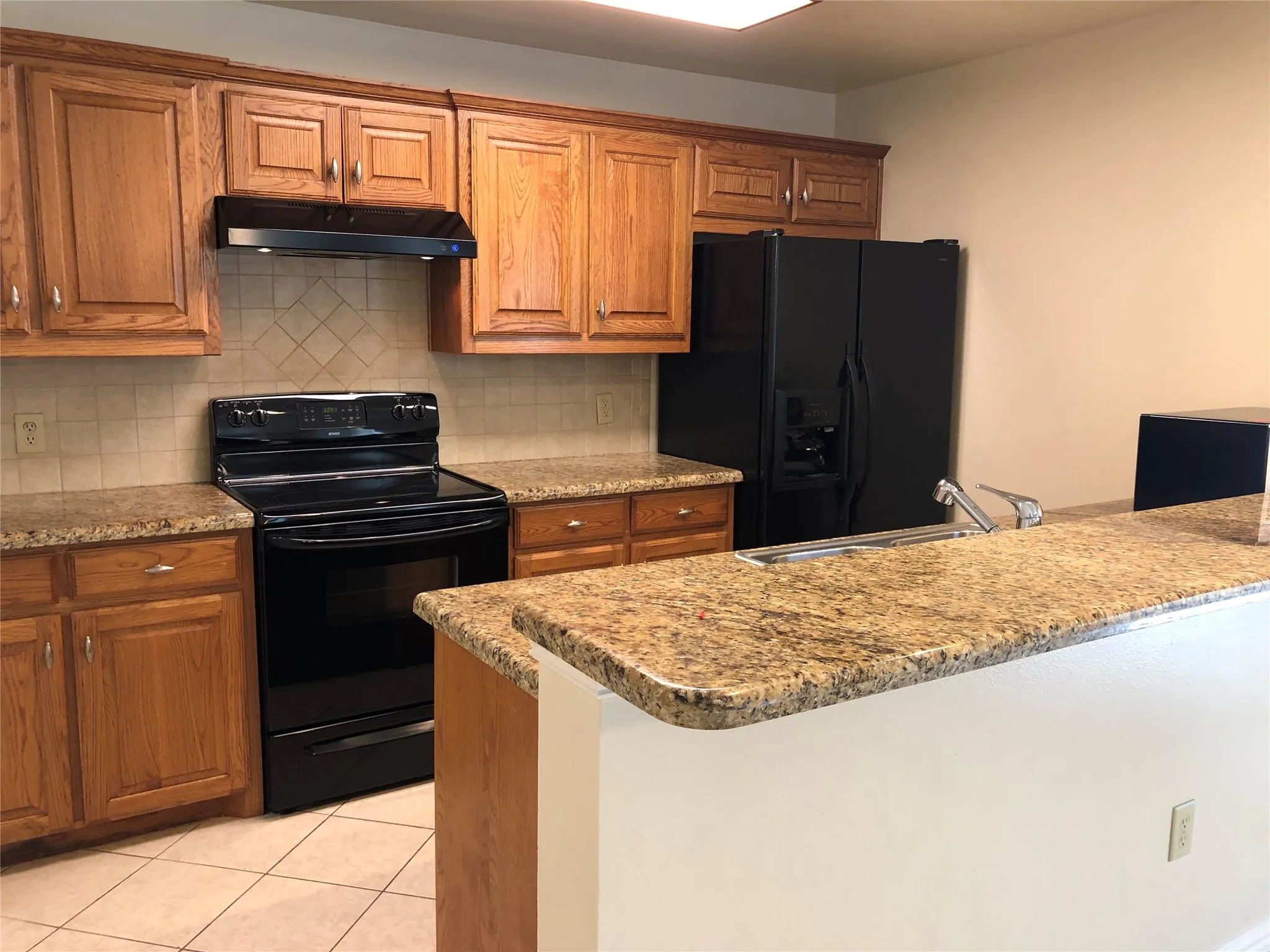 Kitchen featuring wood cabinetry, granite-finish countertops, black appliances, a tile backsplash, and tile flooring