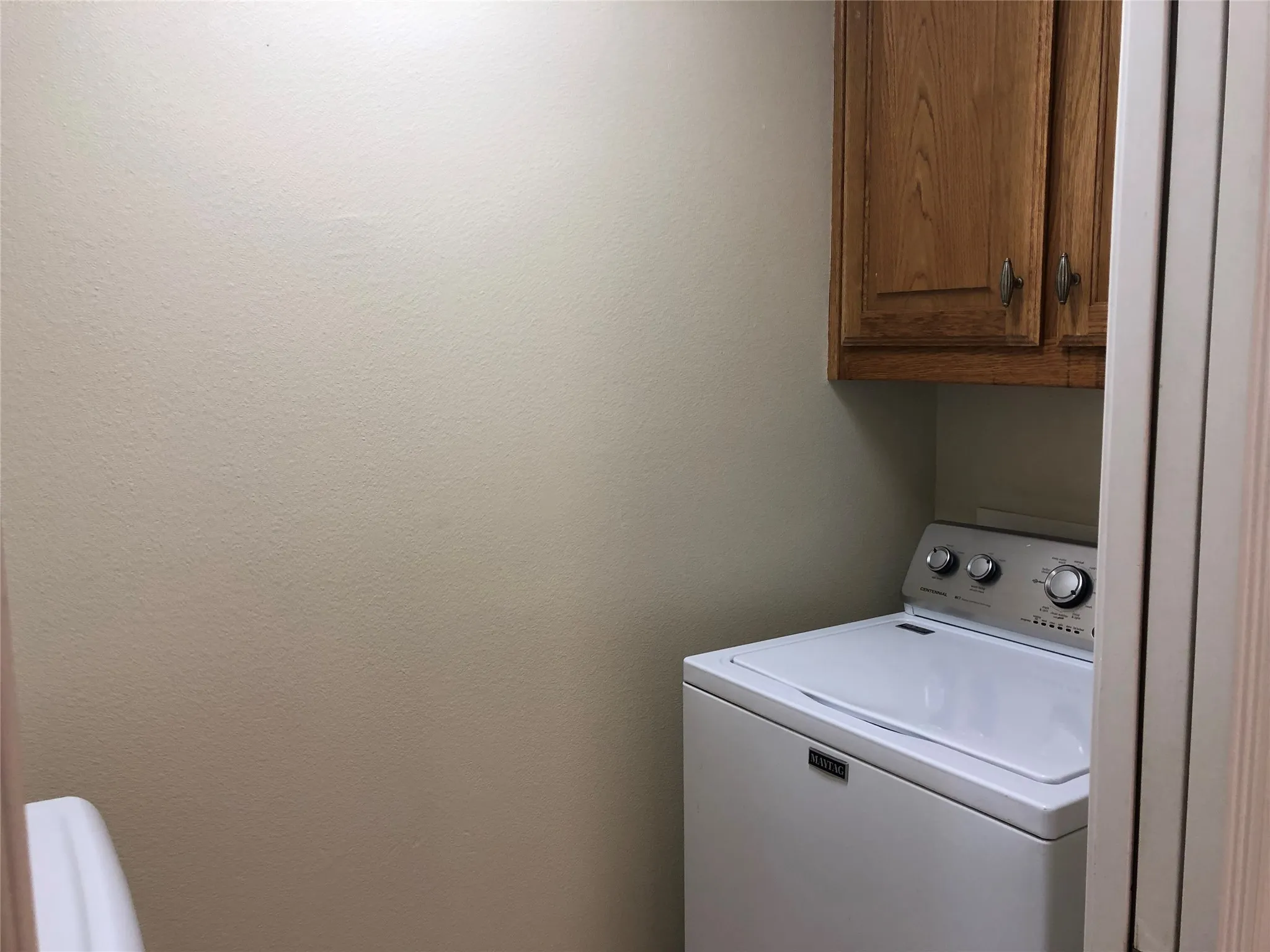 Laundry area featuring neutral wall paint, wood-finish cabinetry with silver hardware, and a built-in appliance space