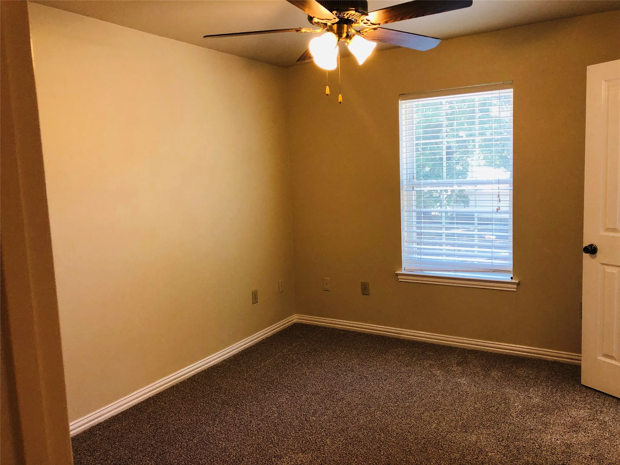 Carpeted room featuring a ceiling fan with light fixture, a window with blinds, and white baseboards