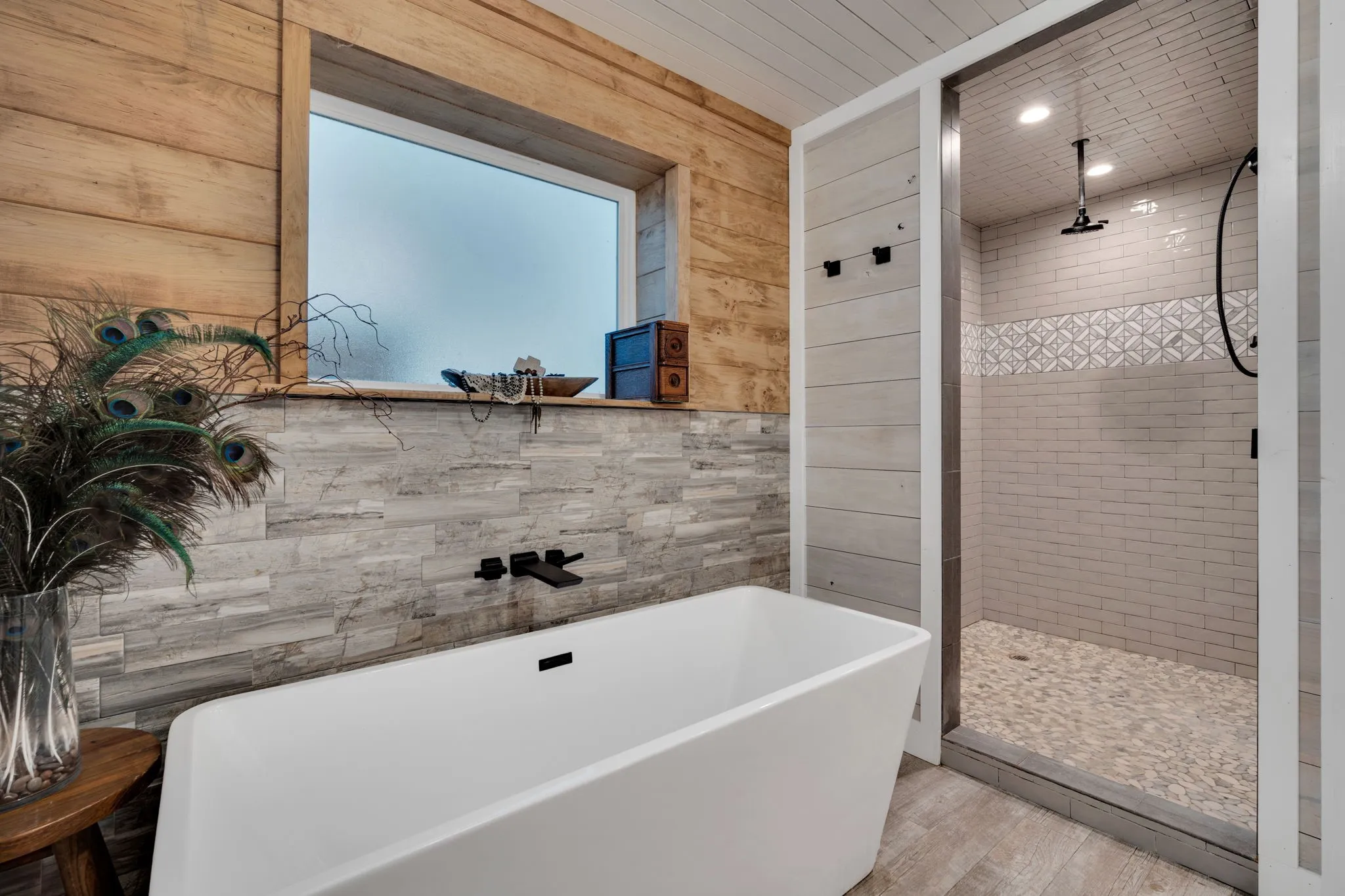 Freestanding soaking tub with wall-mounted matte black faucet, surrounded by wood paneling and stone-look tile