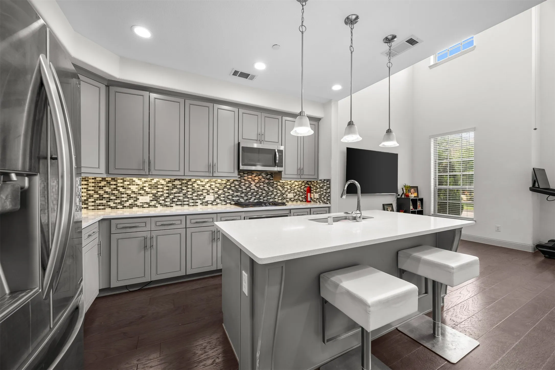 Open-concept kitchen featuring gray shaker-style cabinetry, a mosaic tile backsplash, and a central island with a white countertop and seating