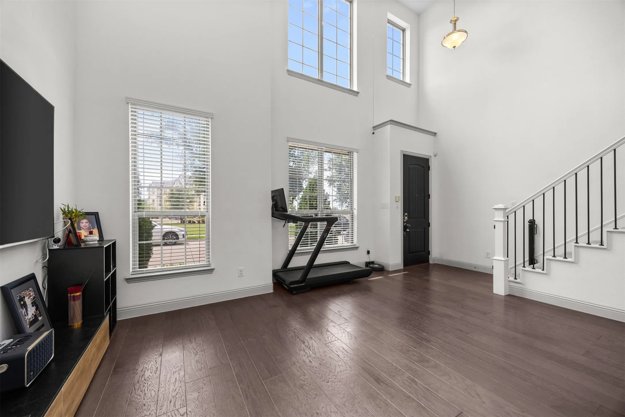 Spacious living area featuring high ceilings, wood-finish flooring, multiple large windows, and a staircase with an iron spindle railing
